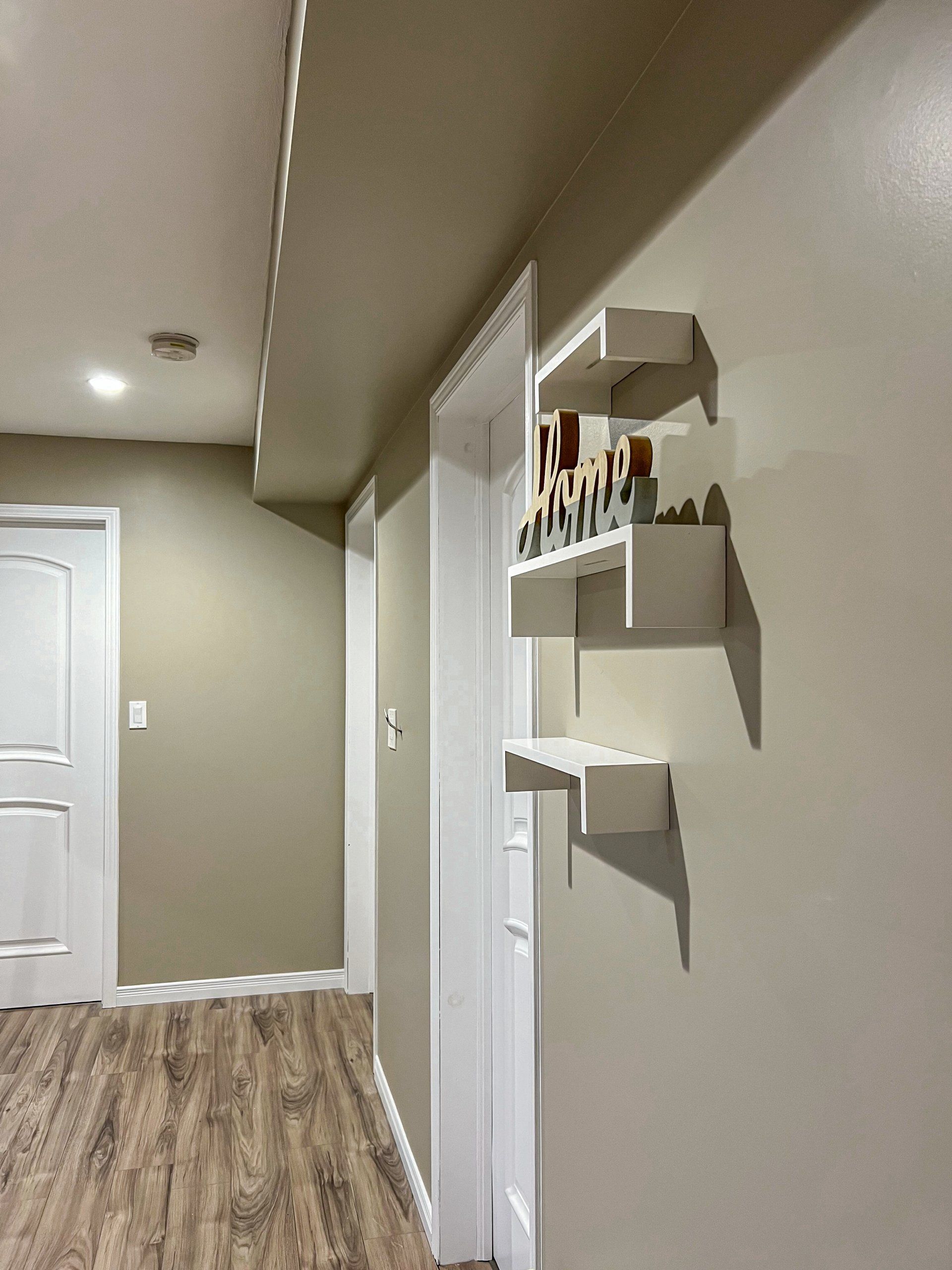 Hallway with beige walls, wood floor, recessed lights, white doors, and small wall shelves with decor.