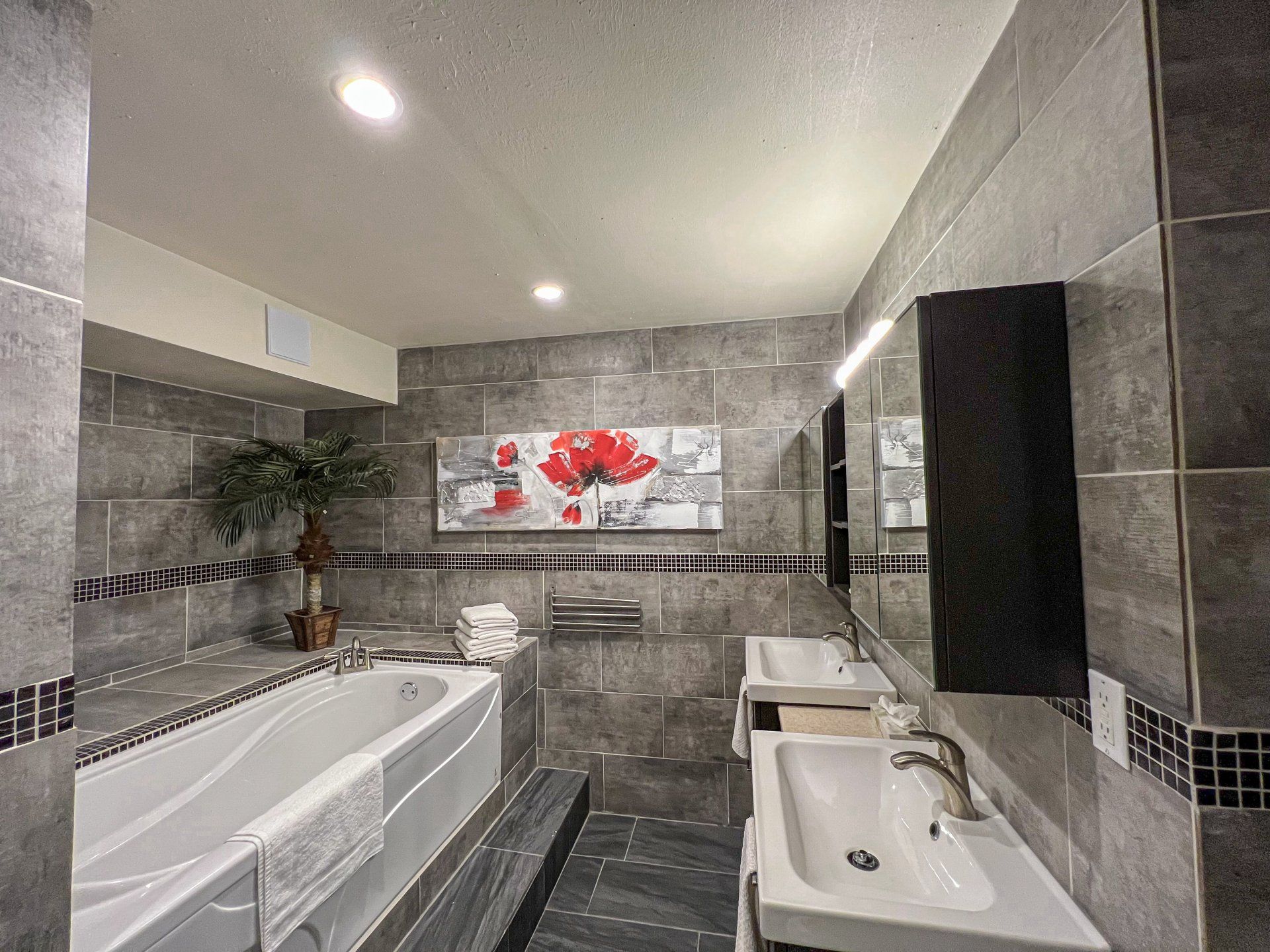 Modern tiled bathroom with bathtub, sink, mirror, and red floral wall art