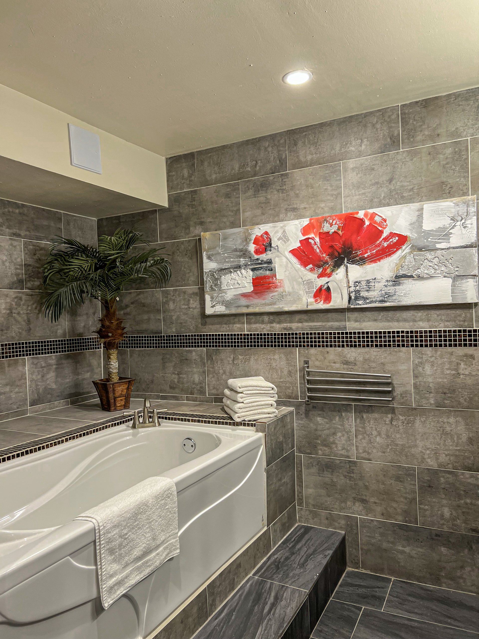 Modern bathroom with a jetted tub, gray tile walls, and red floral wall art