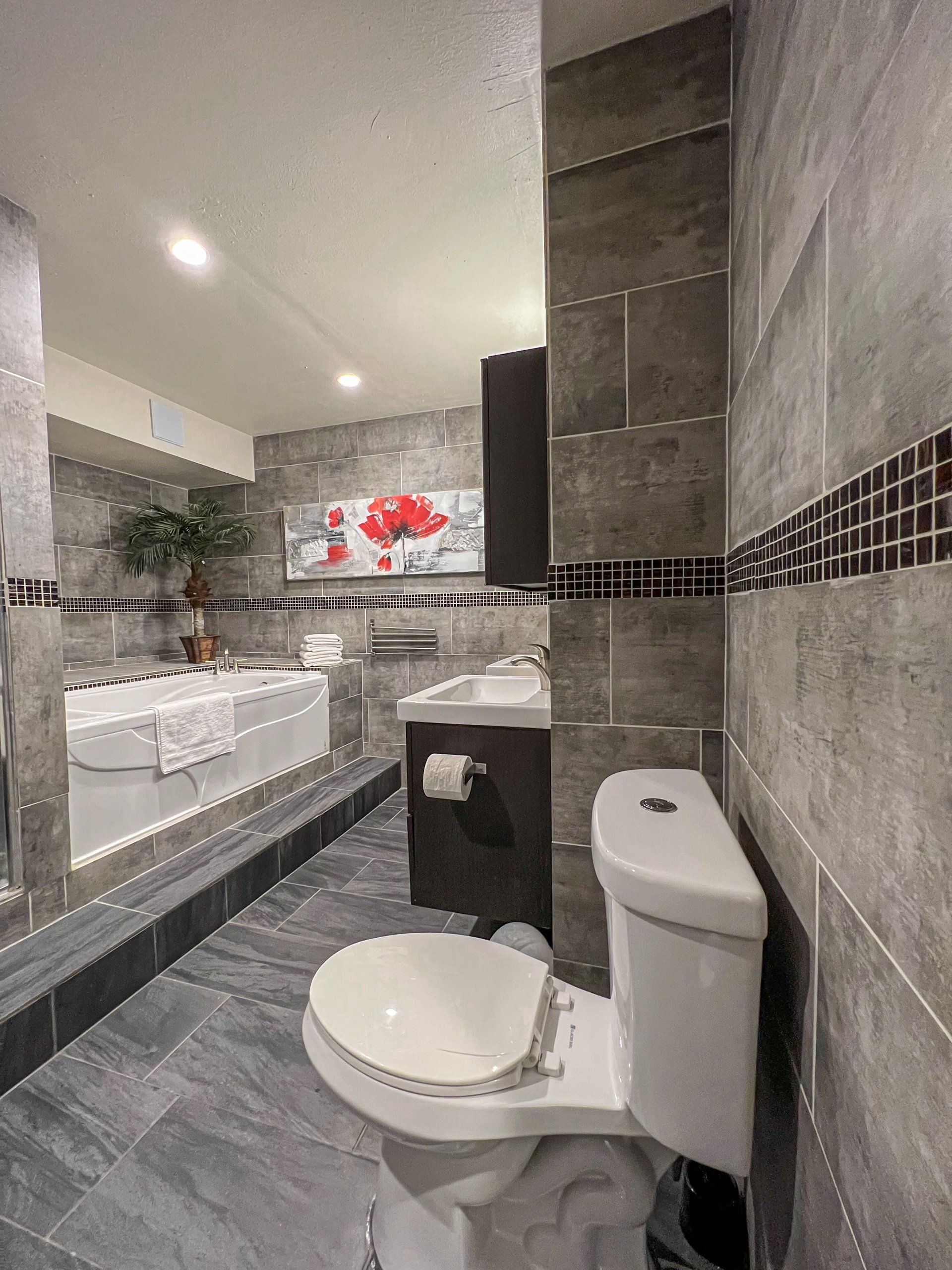 Modern bathroom with toilet, sink, mirror, gray tile, and large vanity area