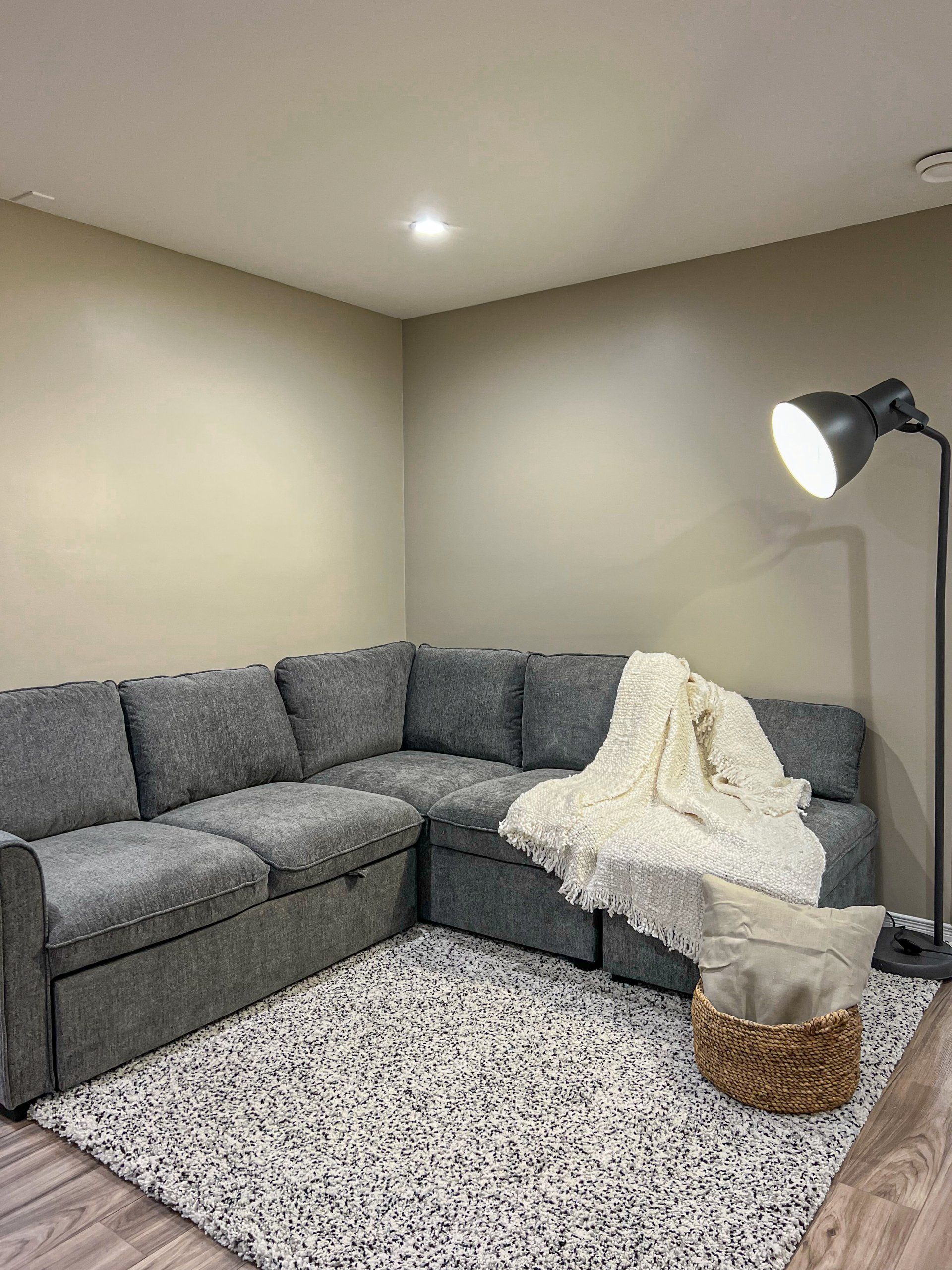 Gray sectional sofa in a corner living room with a white throw blanket and floor lamp on a speckled rug