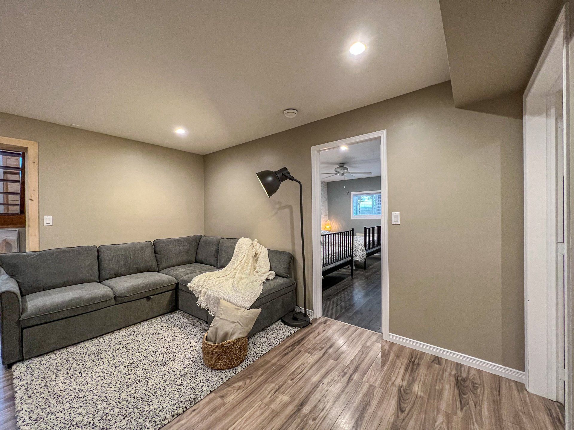 Cozy living room with gray sectional, cream chair, floor lamp, and open doorway to a dining area
