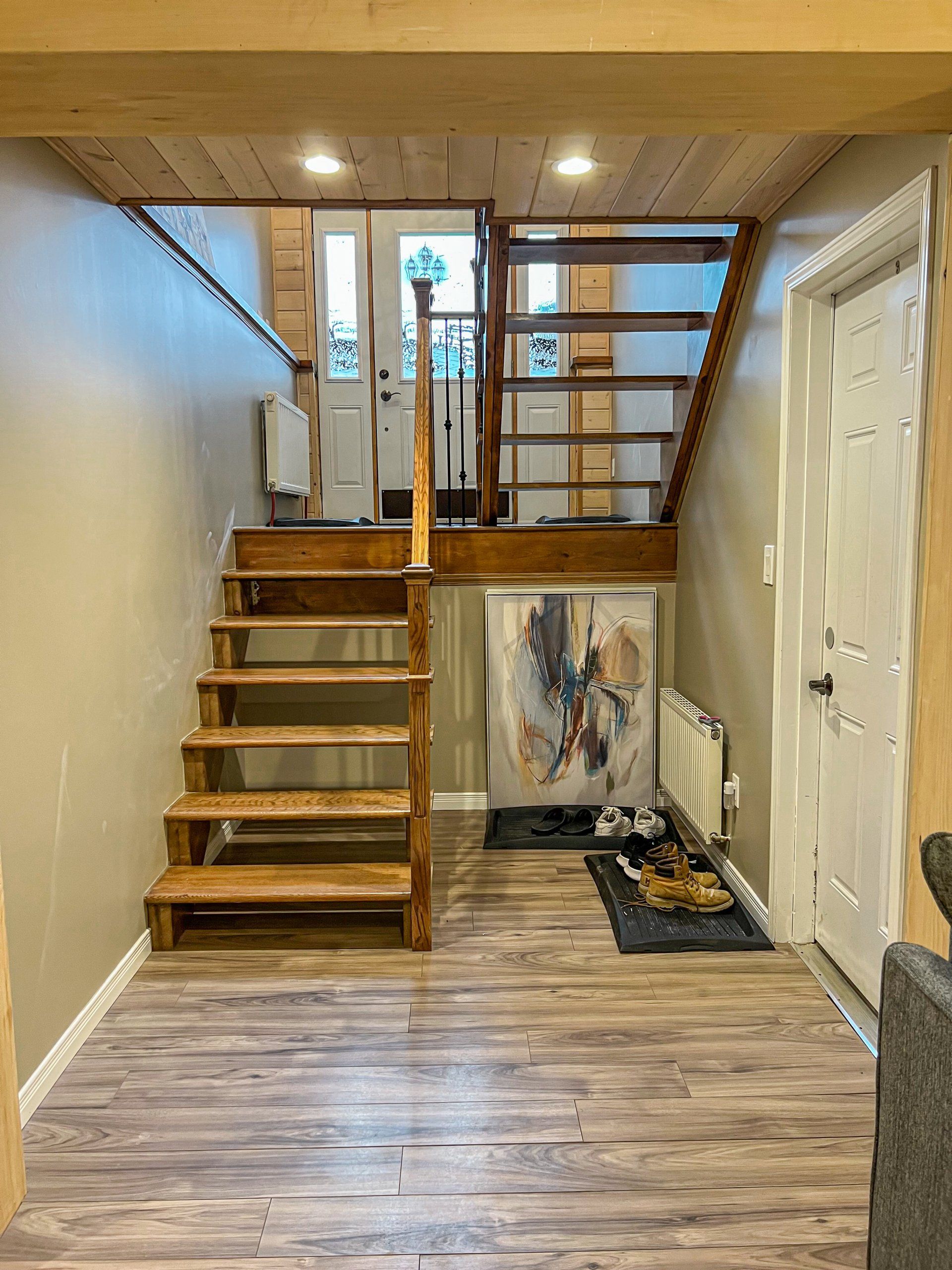 Interior hallway with wooden stairs, railing, white door, and a framed painting against the wall.