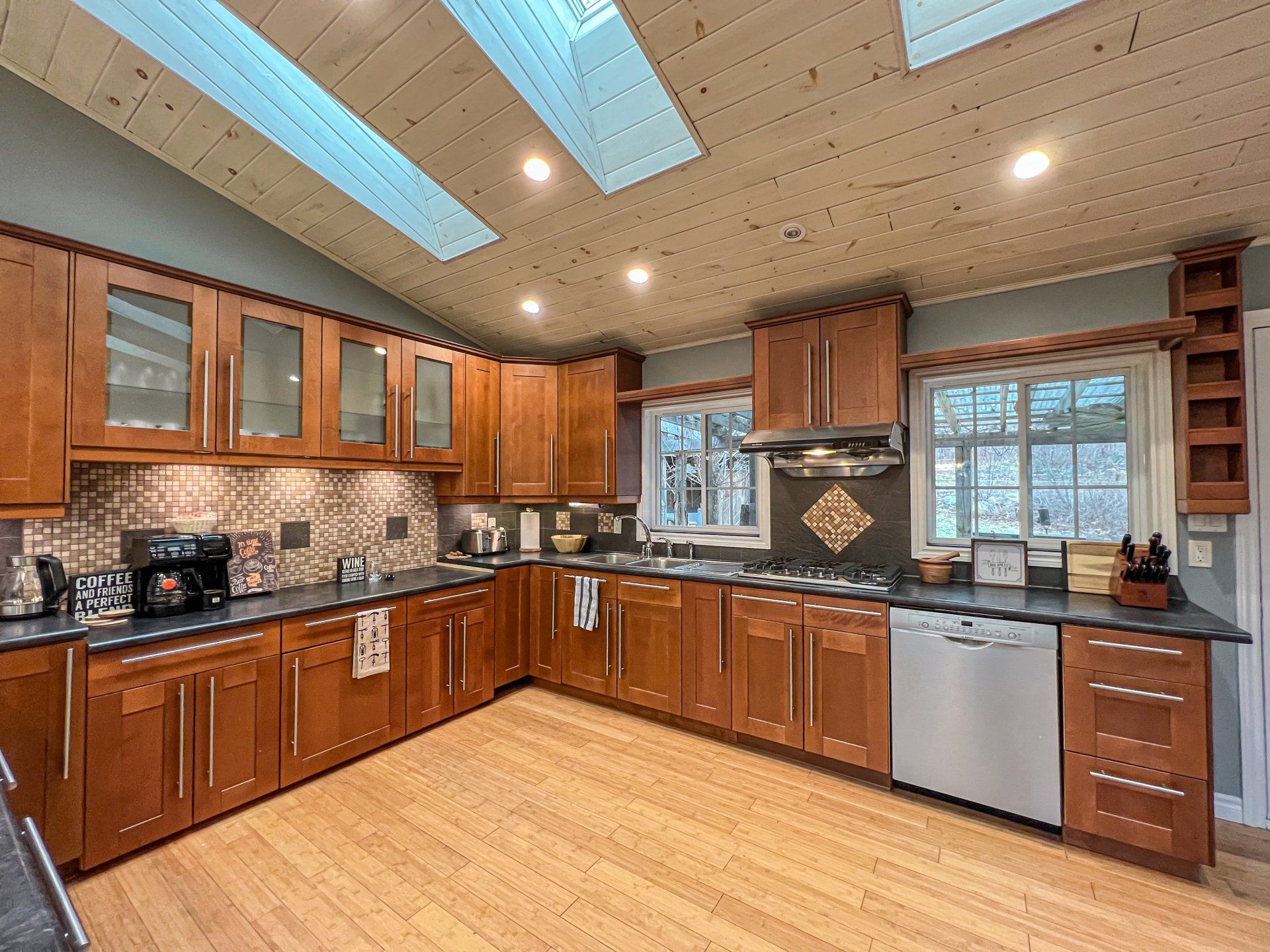 Spacious kitchen with wood cabinets, skylights, tiled backsplash, stainless appliances, and hardwood floor.