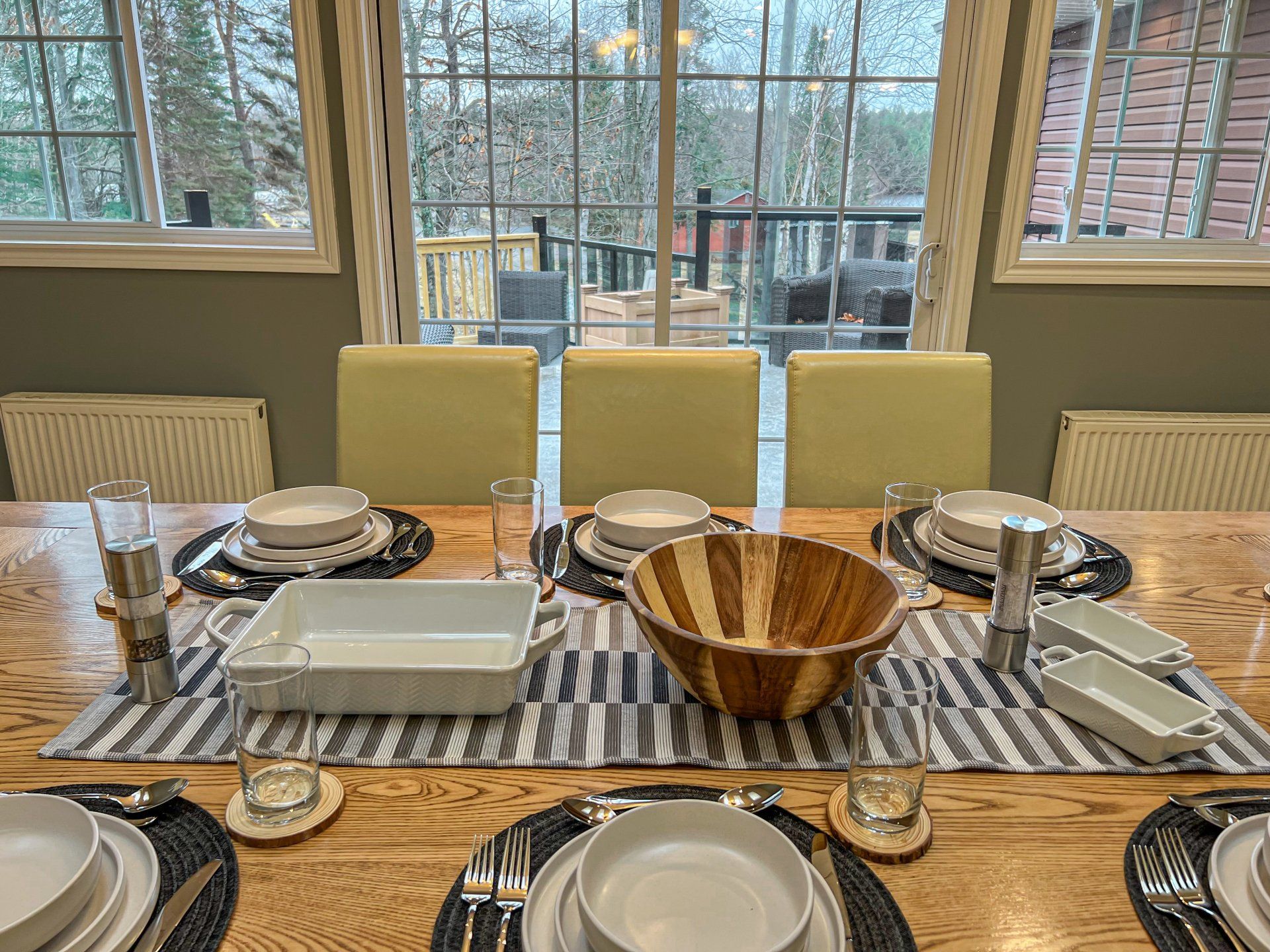 Set dining table with plates, bowls, napkins, and candles by large windows
