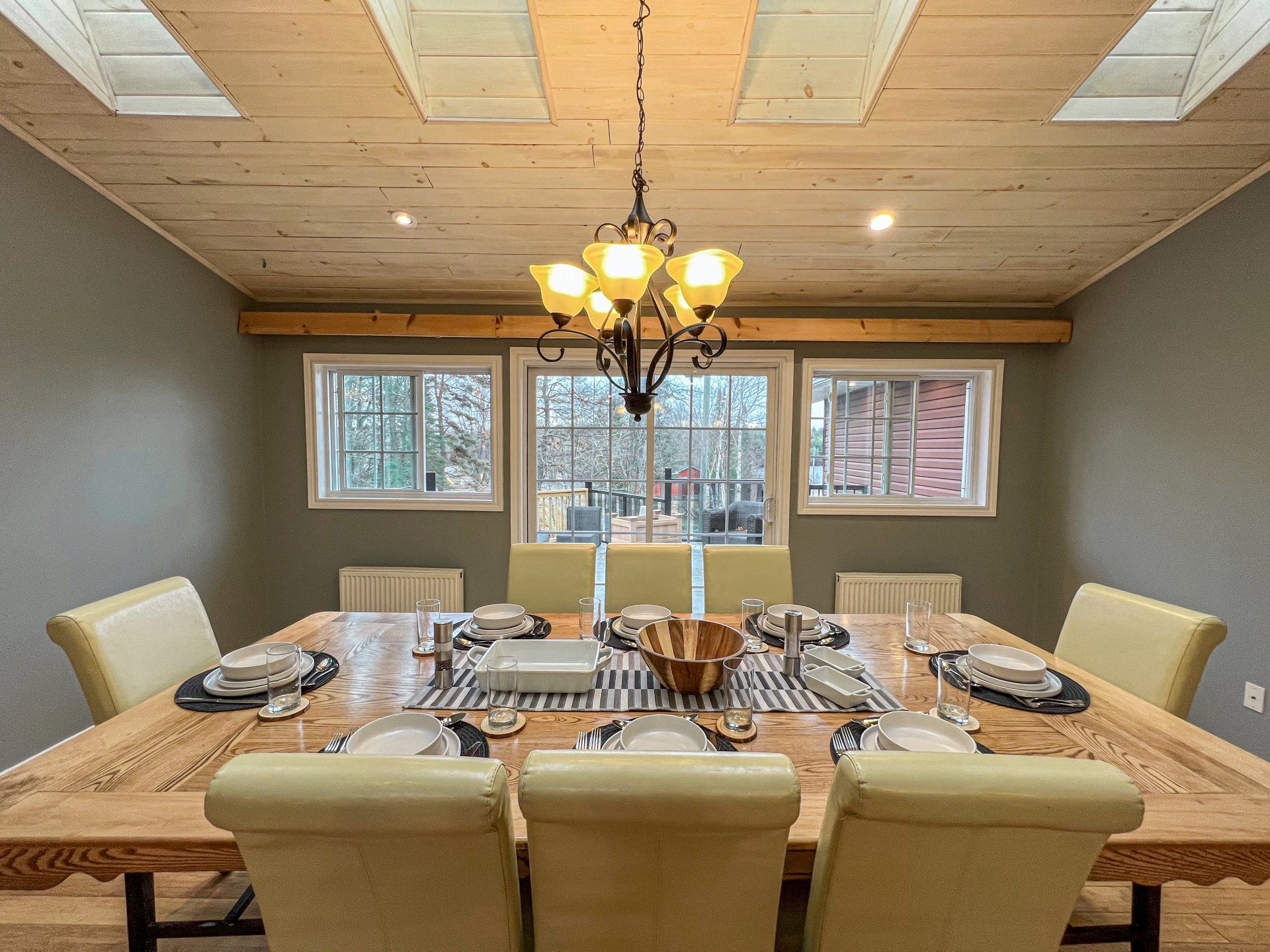 Dining room with a long set table, cream chairs, chandelier, and large windows overlooking snow outside
