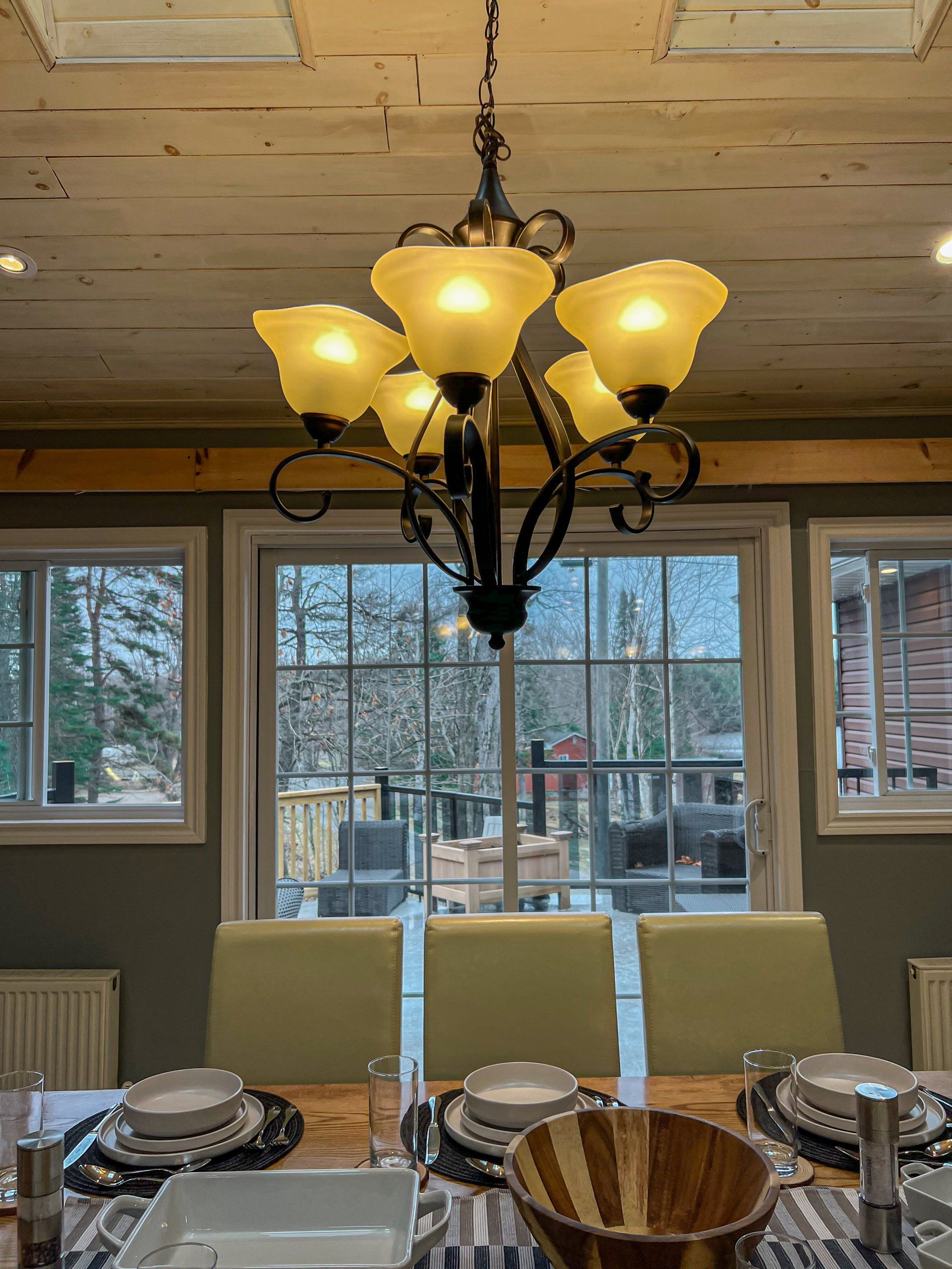 Dining room with a chandelier, large windows, and a set table in a rustic cabin interior