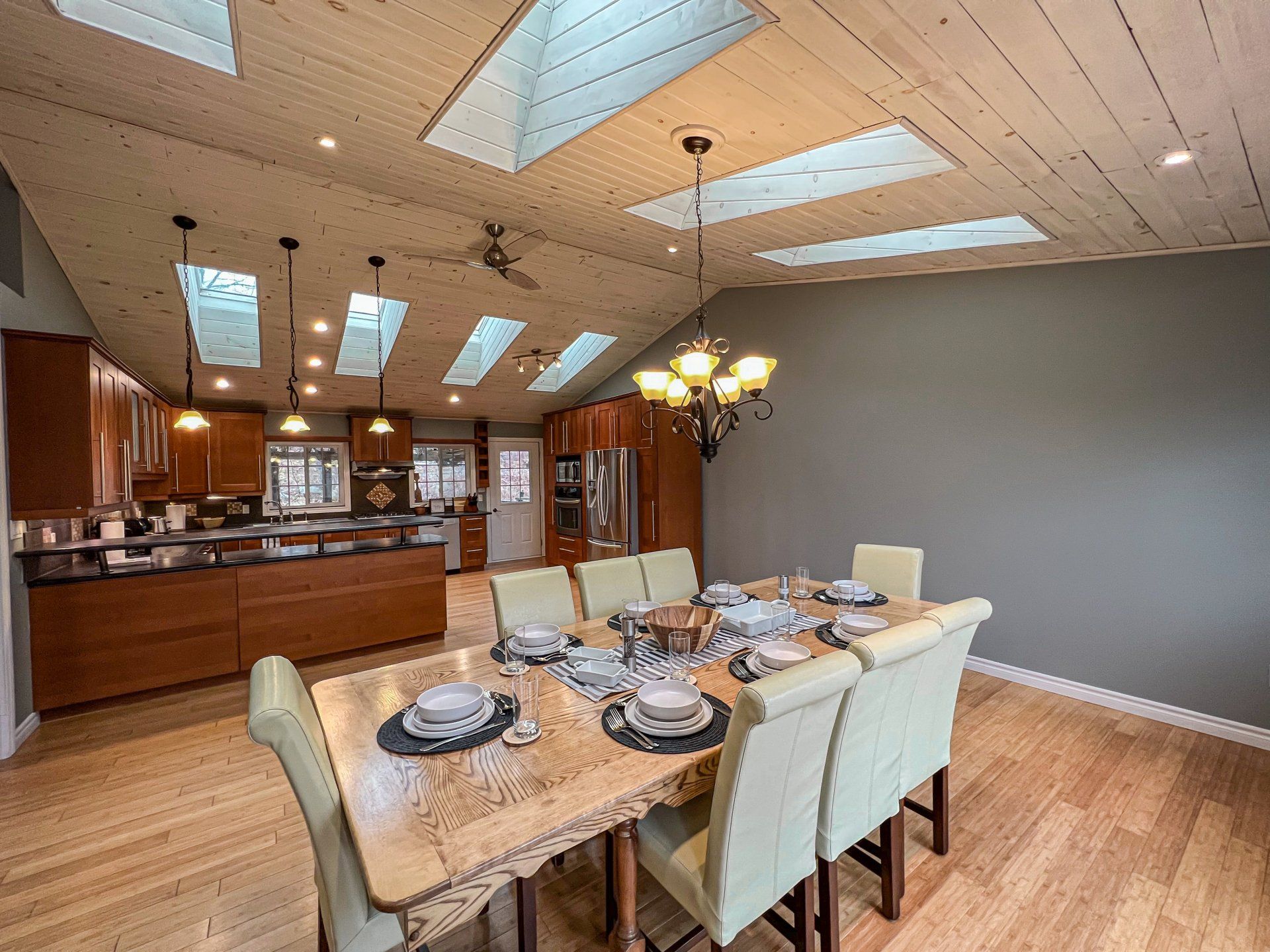 Dining room with set table, chandelier, wood floors, and open kitchen/bar in the background