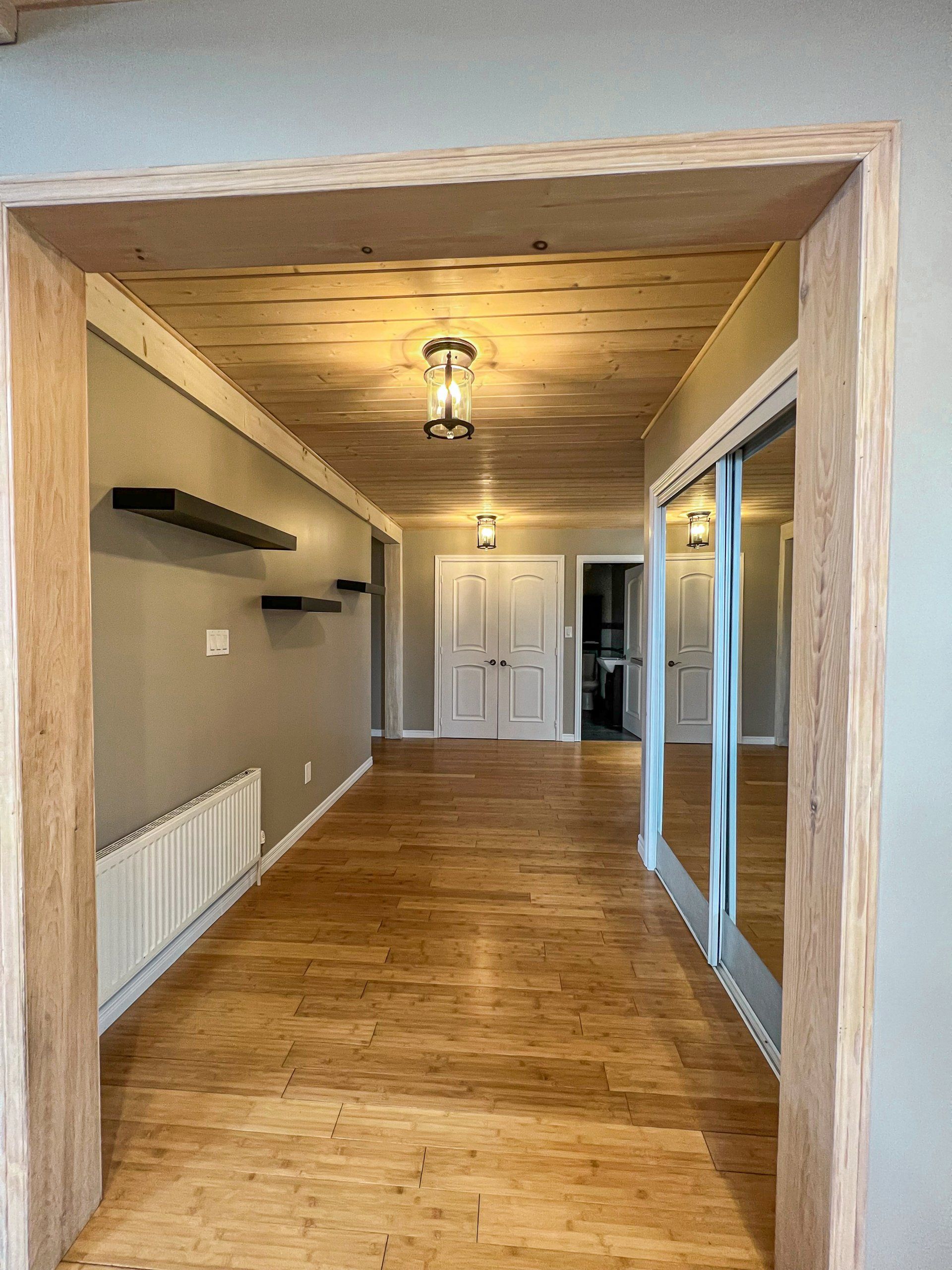 Empty narrow hallway with wood floors, beige walls, ceiling lights, and sliding glass doors on the right