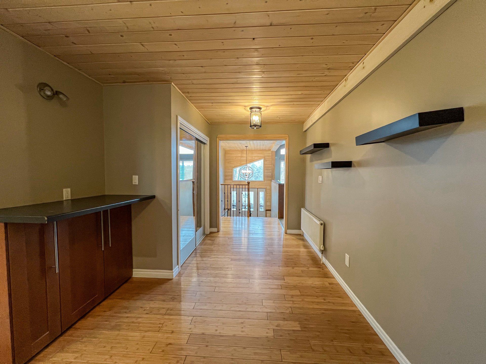Empty hallway with wood ceiling and floors, white walls, and a small kitchen counter on the left.