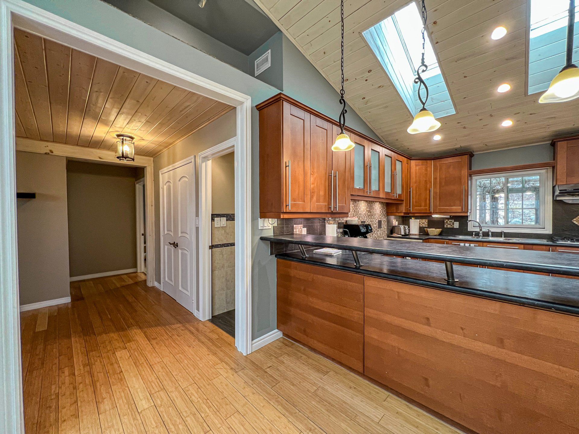 Modern kitchen with wood cabinets, granite island, and adjacent hallway with wood floors and white trim
