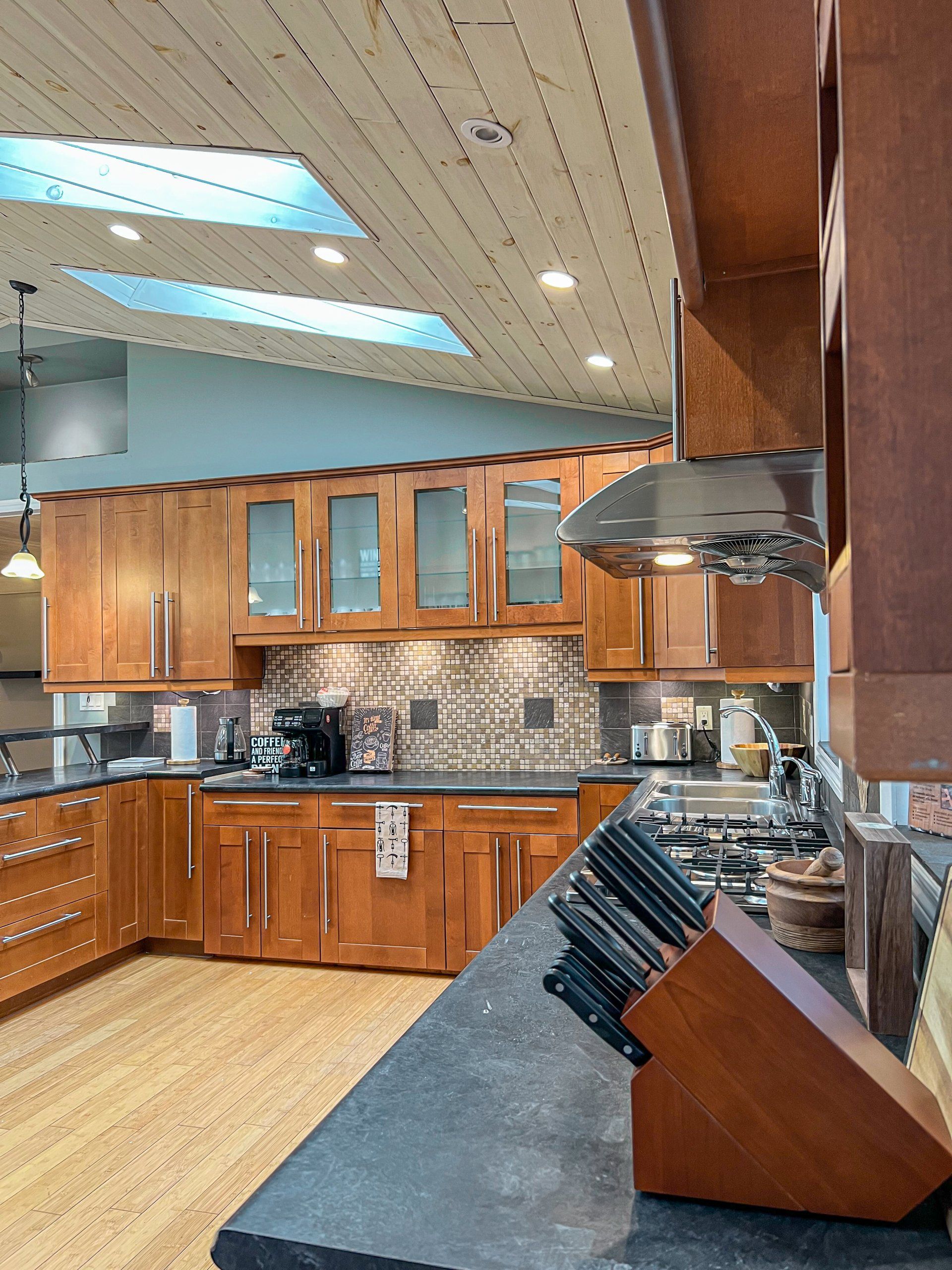 Modern kitchen with wood cabinets, granite counters, stainless range hood, and mosaic tile backsplash
