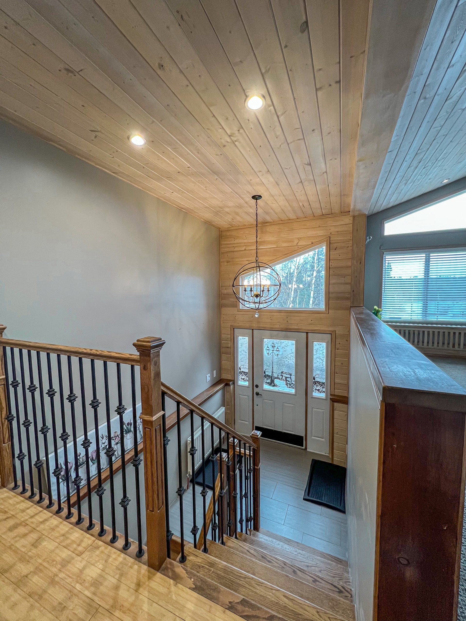 Interior staircase with wooden railing, skylight, and glass front door in a bright entryway
