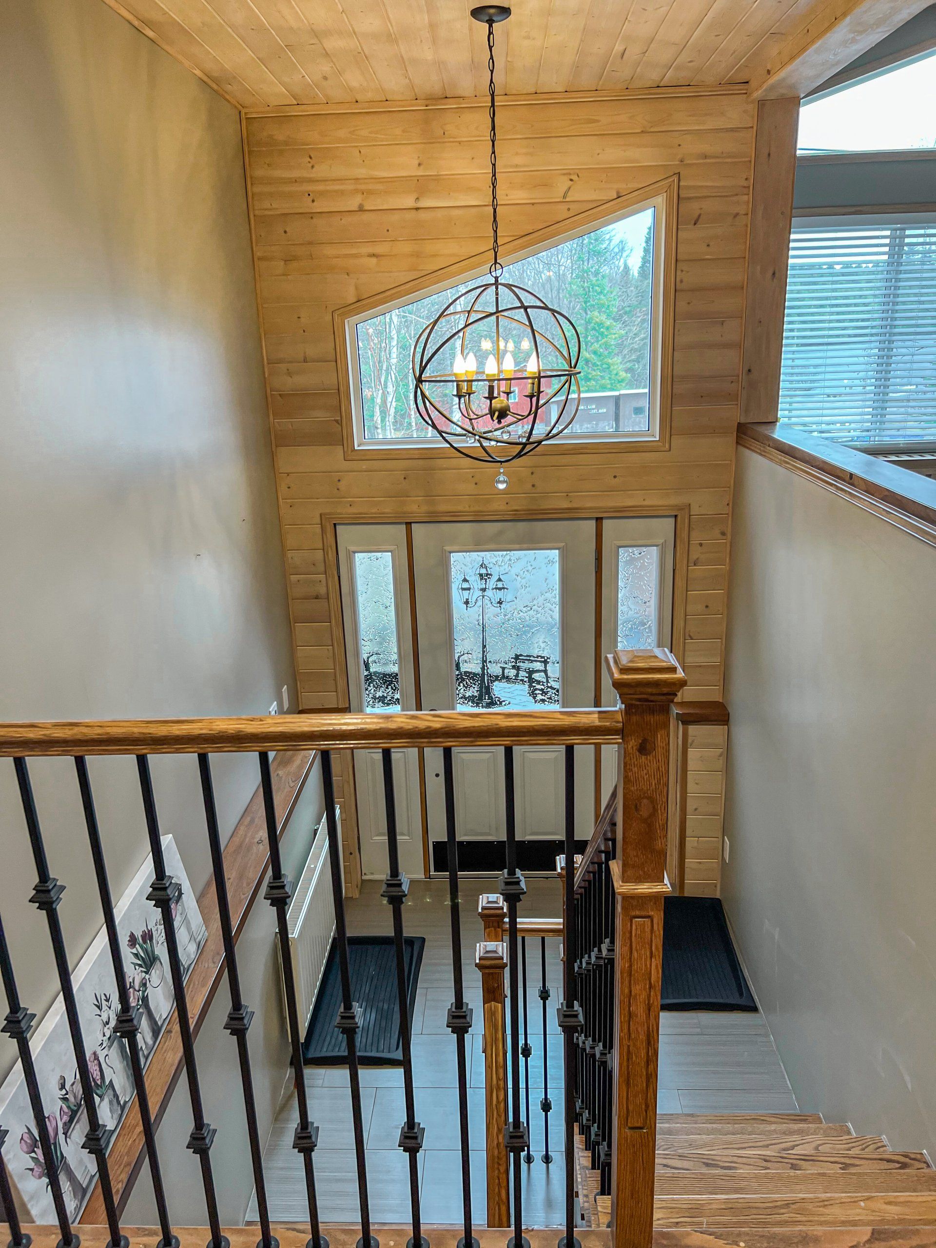 Wood-paneled foyer with staircase railing, chandelier, and triangular window above the front door