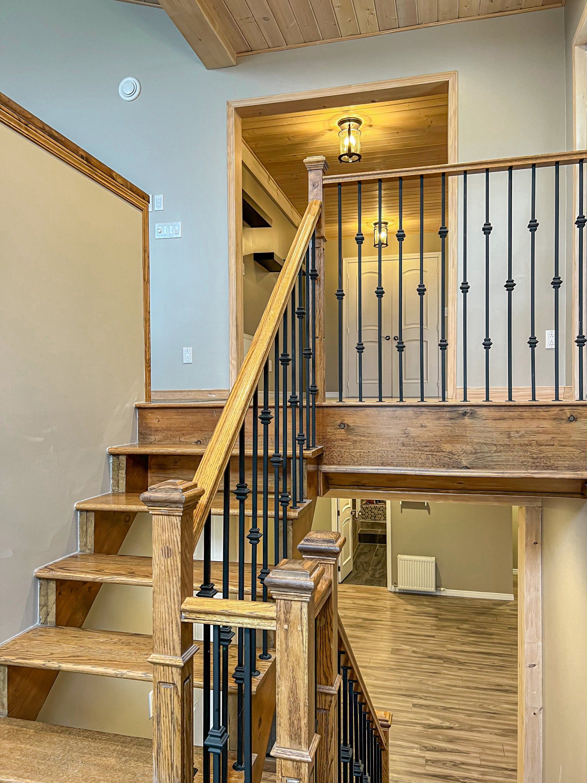 Staircase with wooden steps, black iron railing, and beige walls in a split-level interior