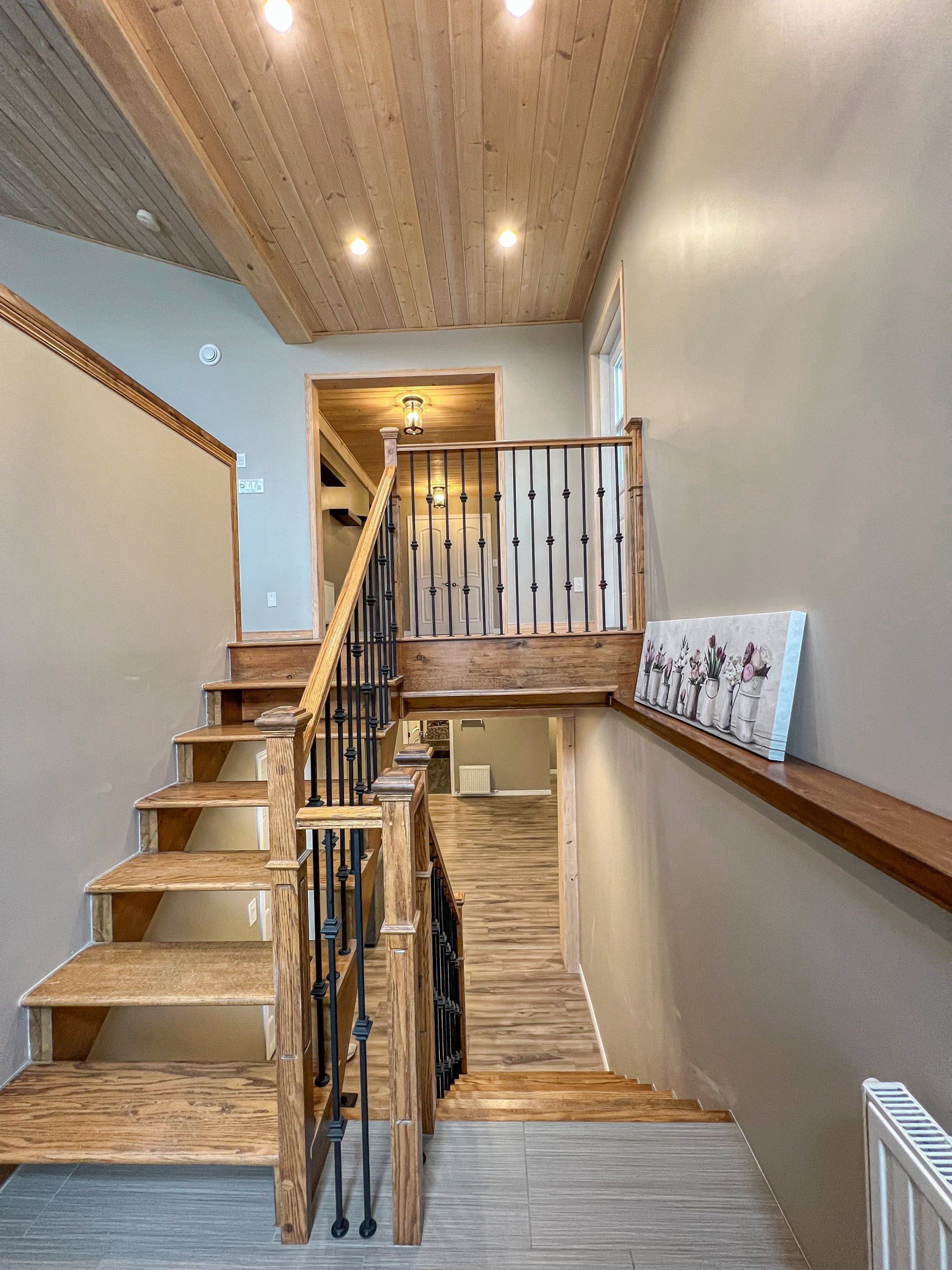 Indoor staircase with wooden steps, black railing, and a lit ceiling in a narrow hallway