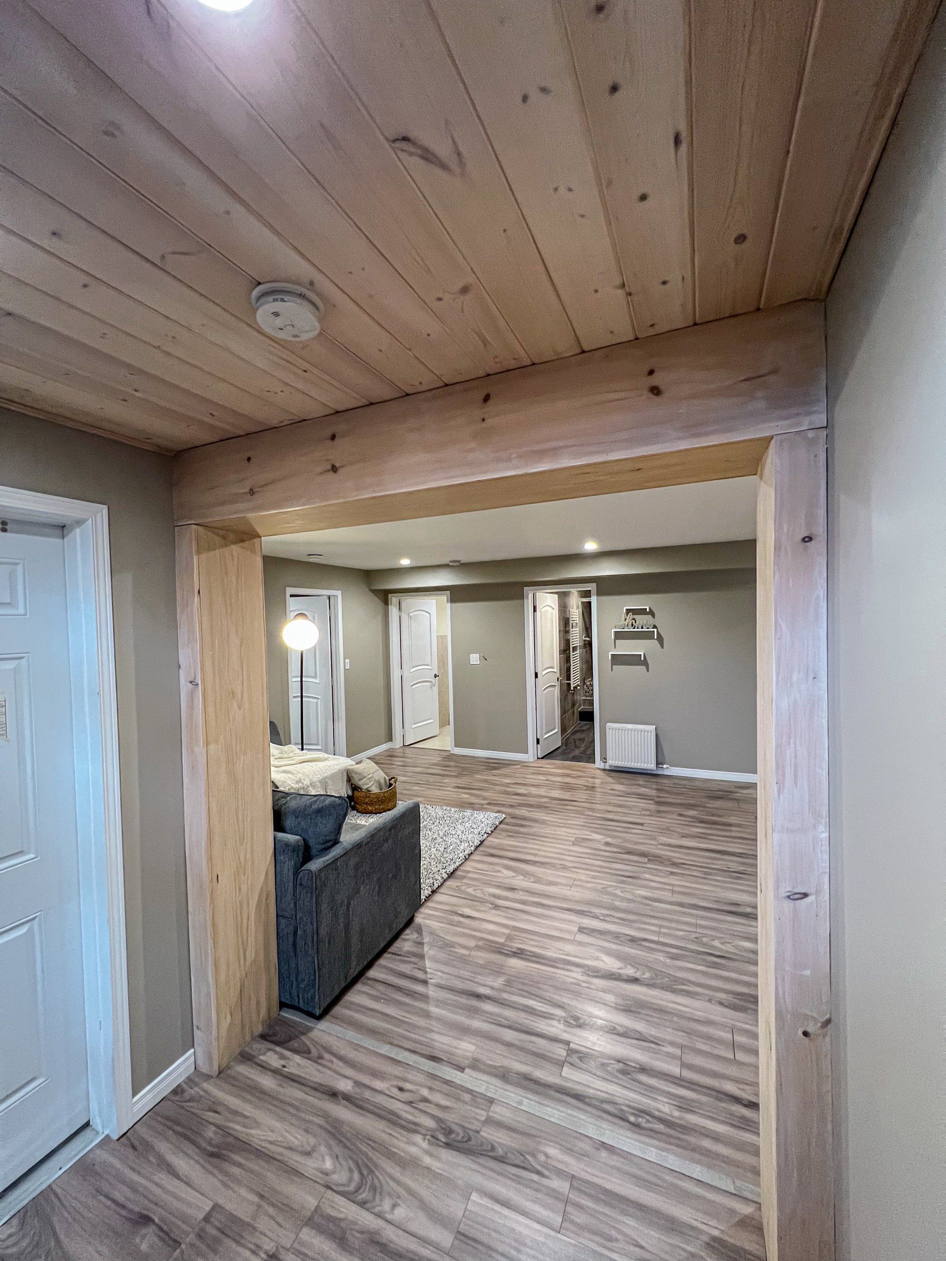 Wood-paneled hallway opening to a living room with gray sofa, patterned rug, and wood-look flooring.