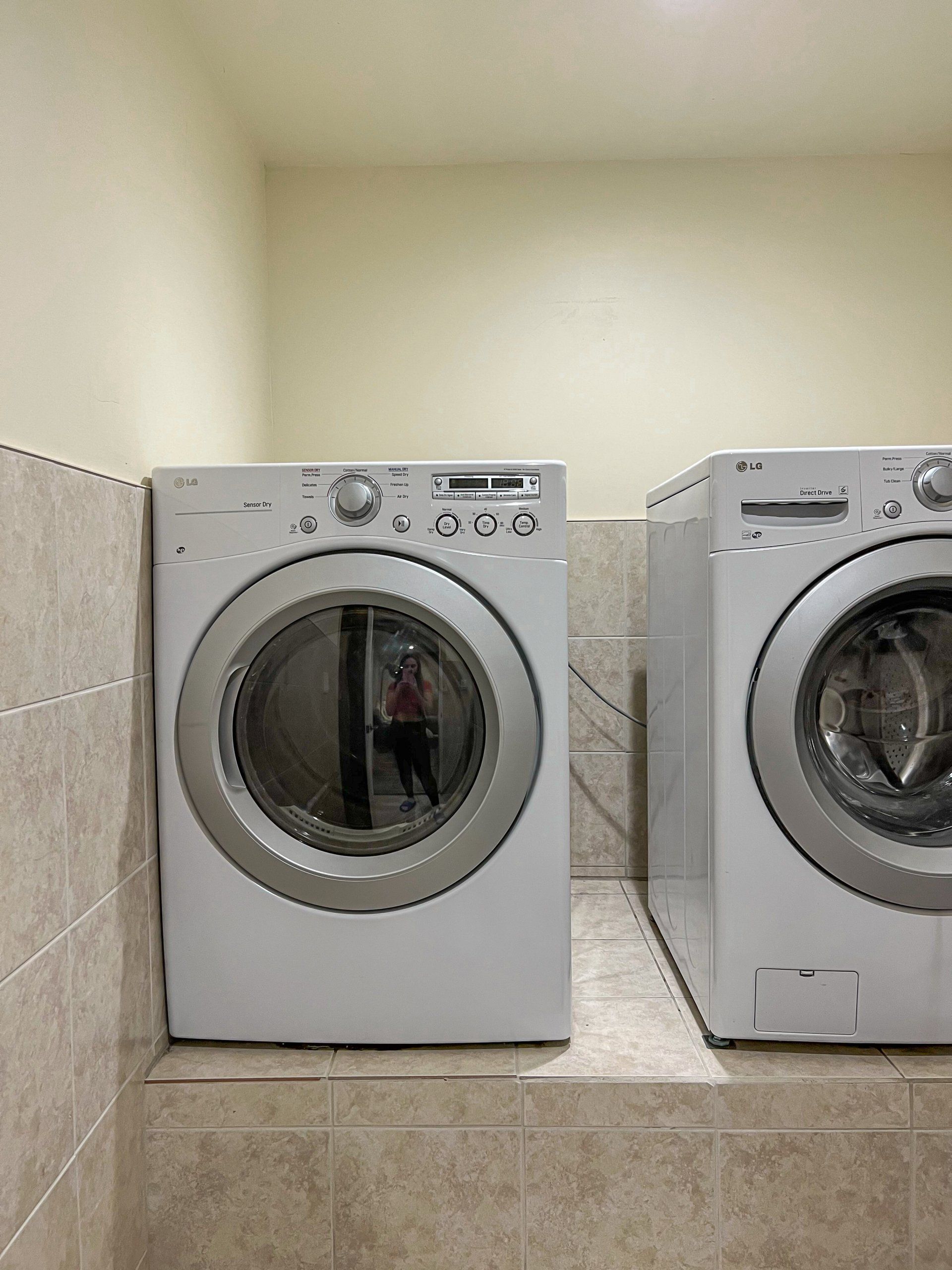 Two front-loading washing machines in a tiled laundry room, one silver and one white.
