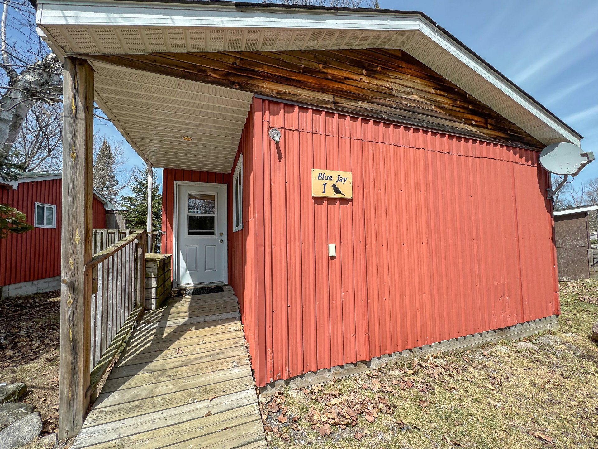 Red building with a covered wooden porch and white door under a slanted roof