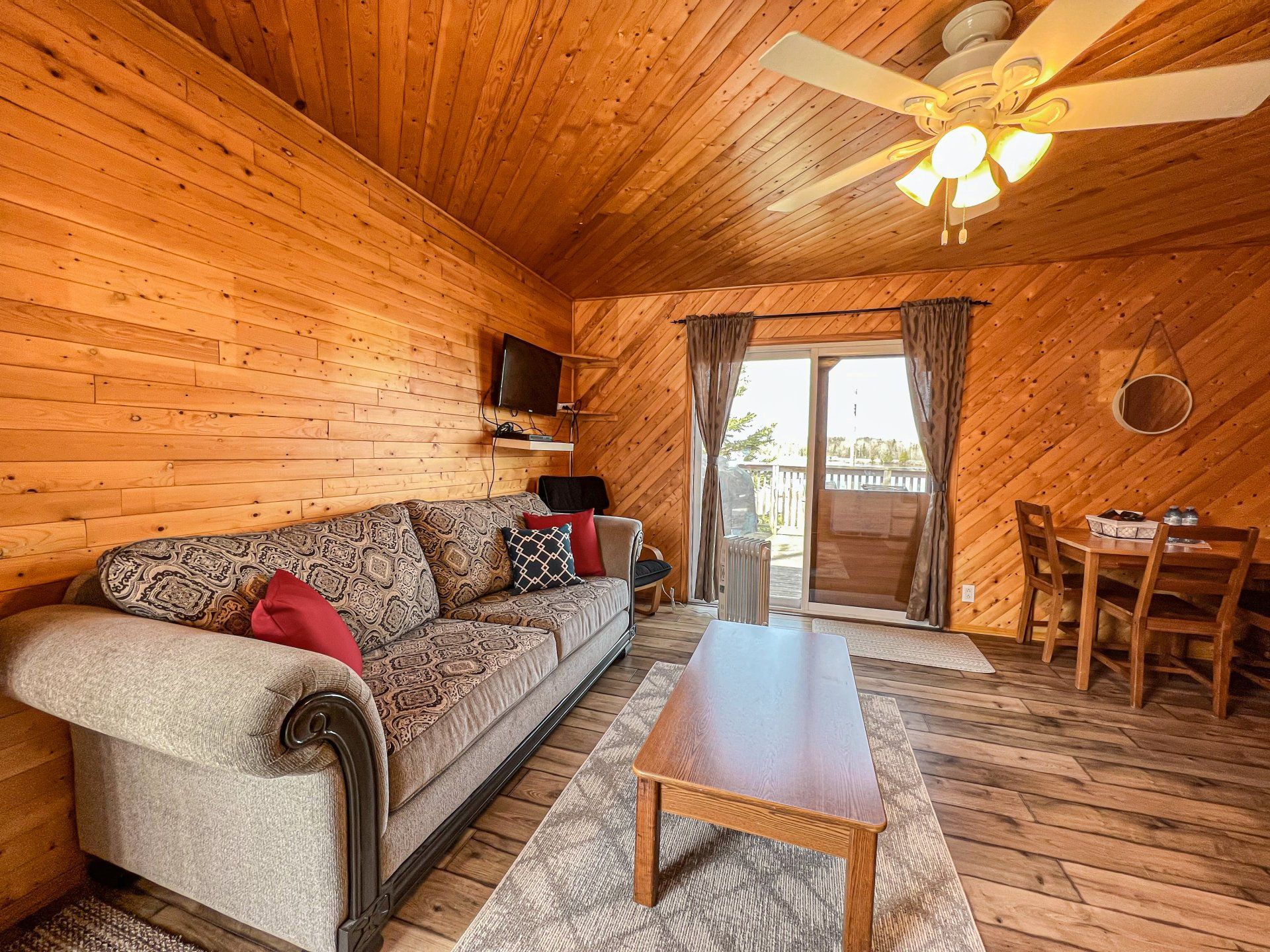 Cozy log cabin living room with sofa, coffee table, dining nook, and open glass doors to a deck.