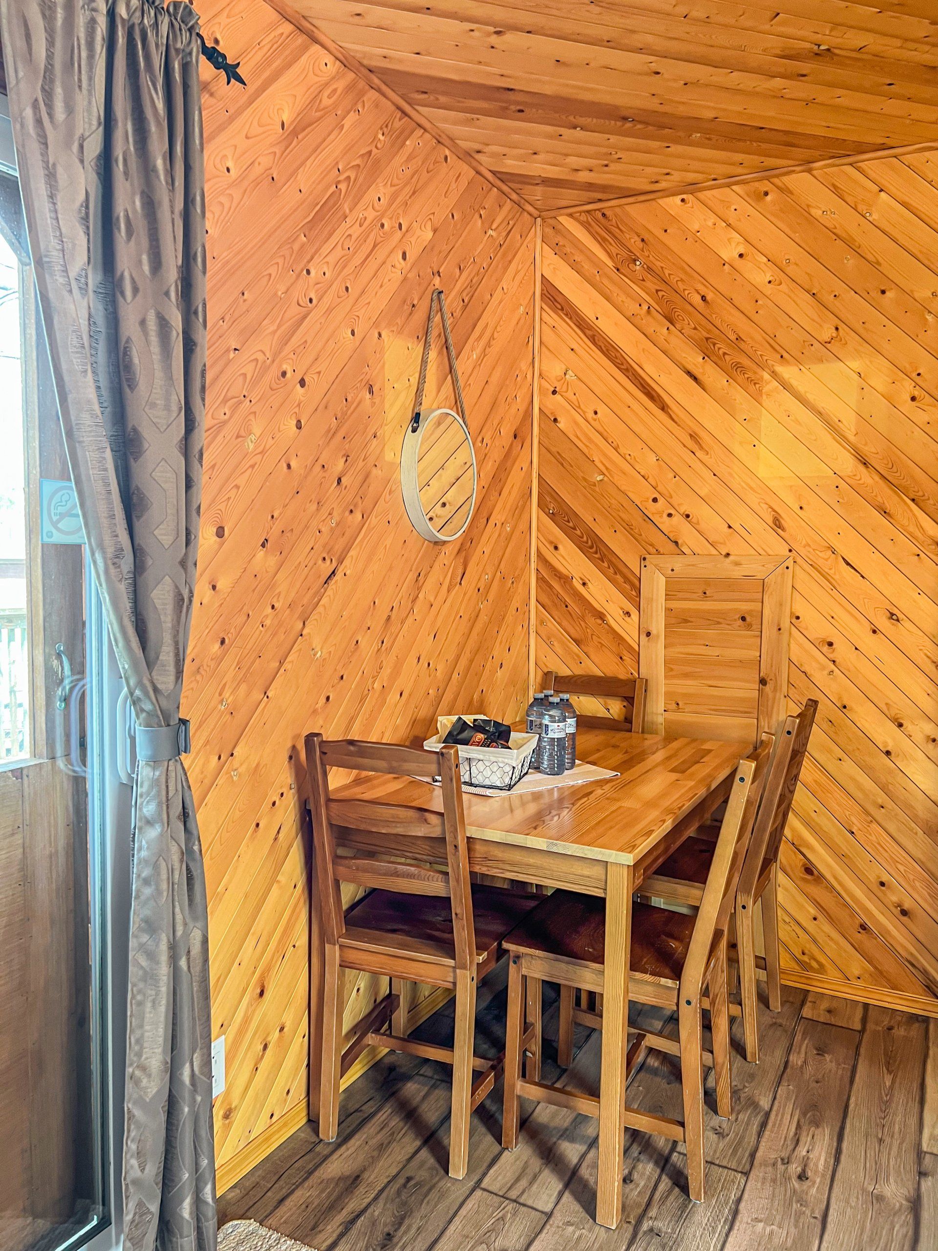 Cozy wood-paneled nook with a small table, two chairs, and a curtain by a window.