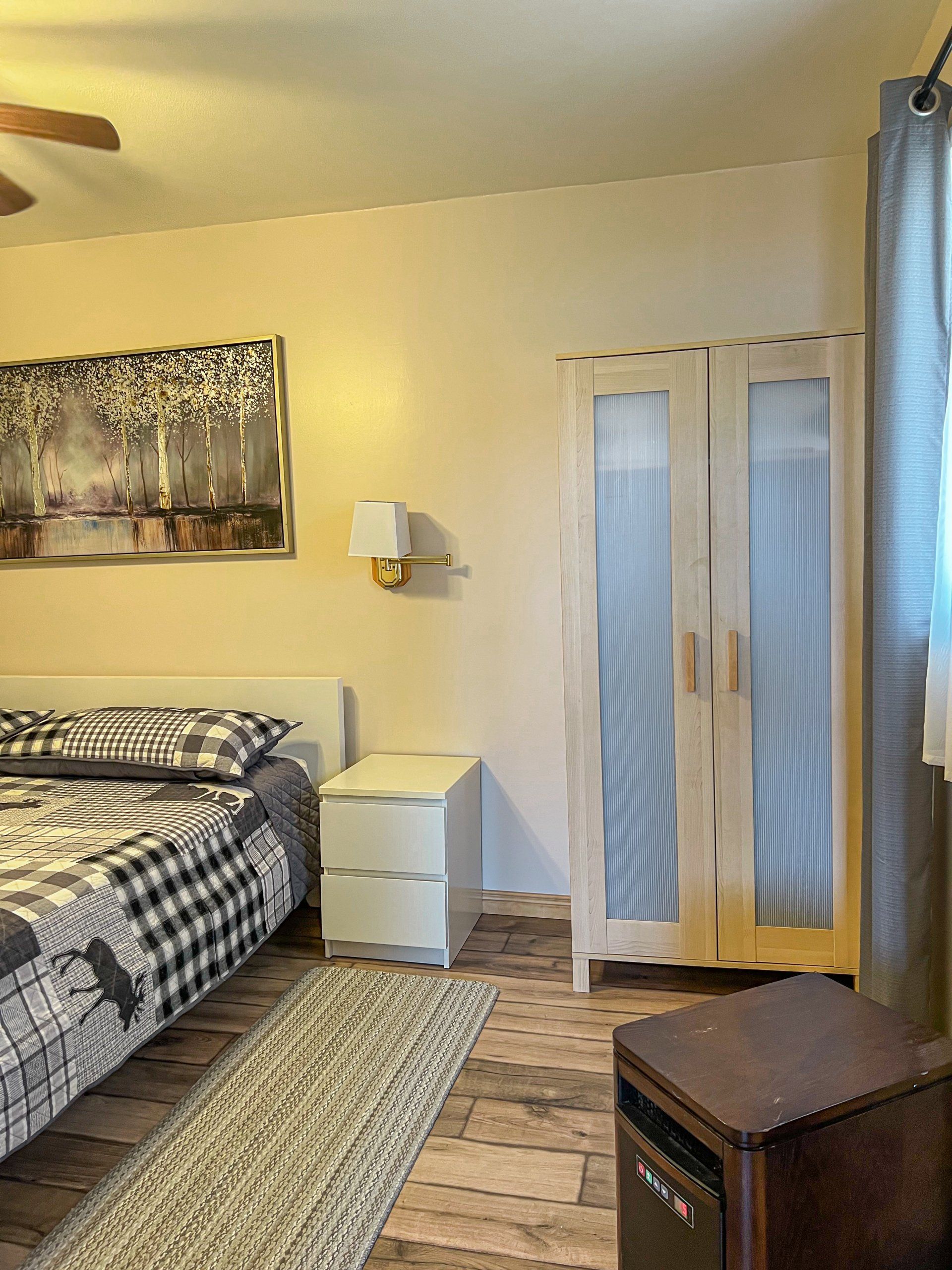 Bedroom with bed, nightstand, wardrobe, rug, and window curtains in warm lighting