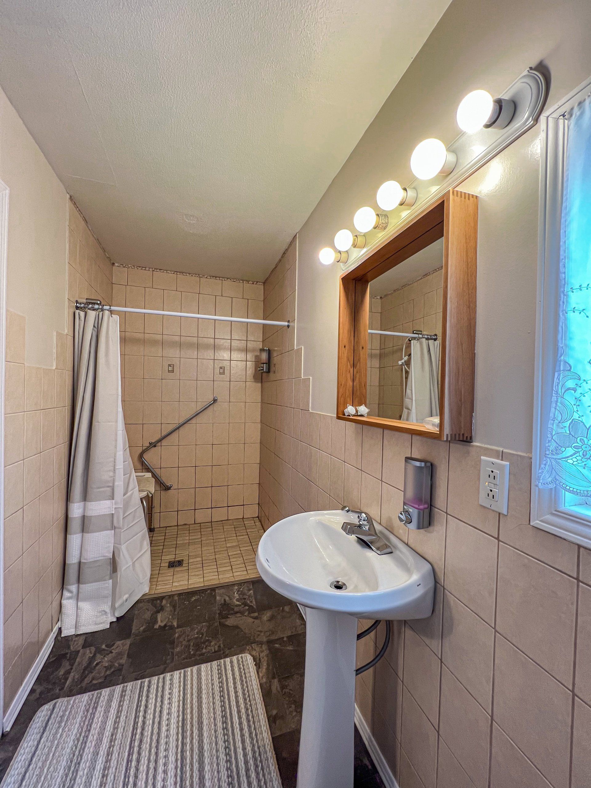 Small beige bathroom with a pedestal sink, mirror lights, tiled shower, and striped towel.