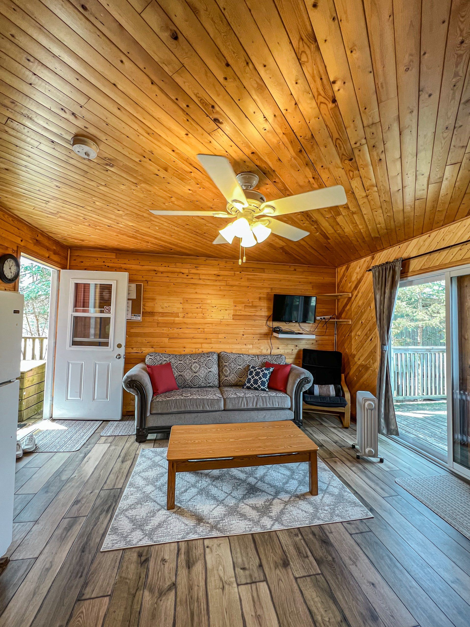 Cozy wood-paneled living room with sofa, coffee table, ceiling fan, TV, and sliding glass door