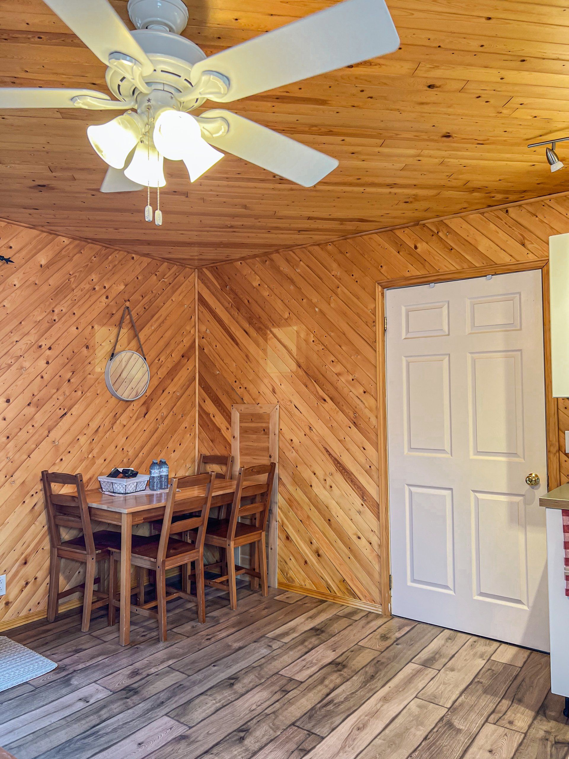 Wood-paneled dining room with ceiling fan, table and chairs, and a white door