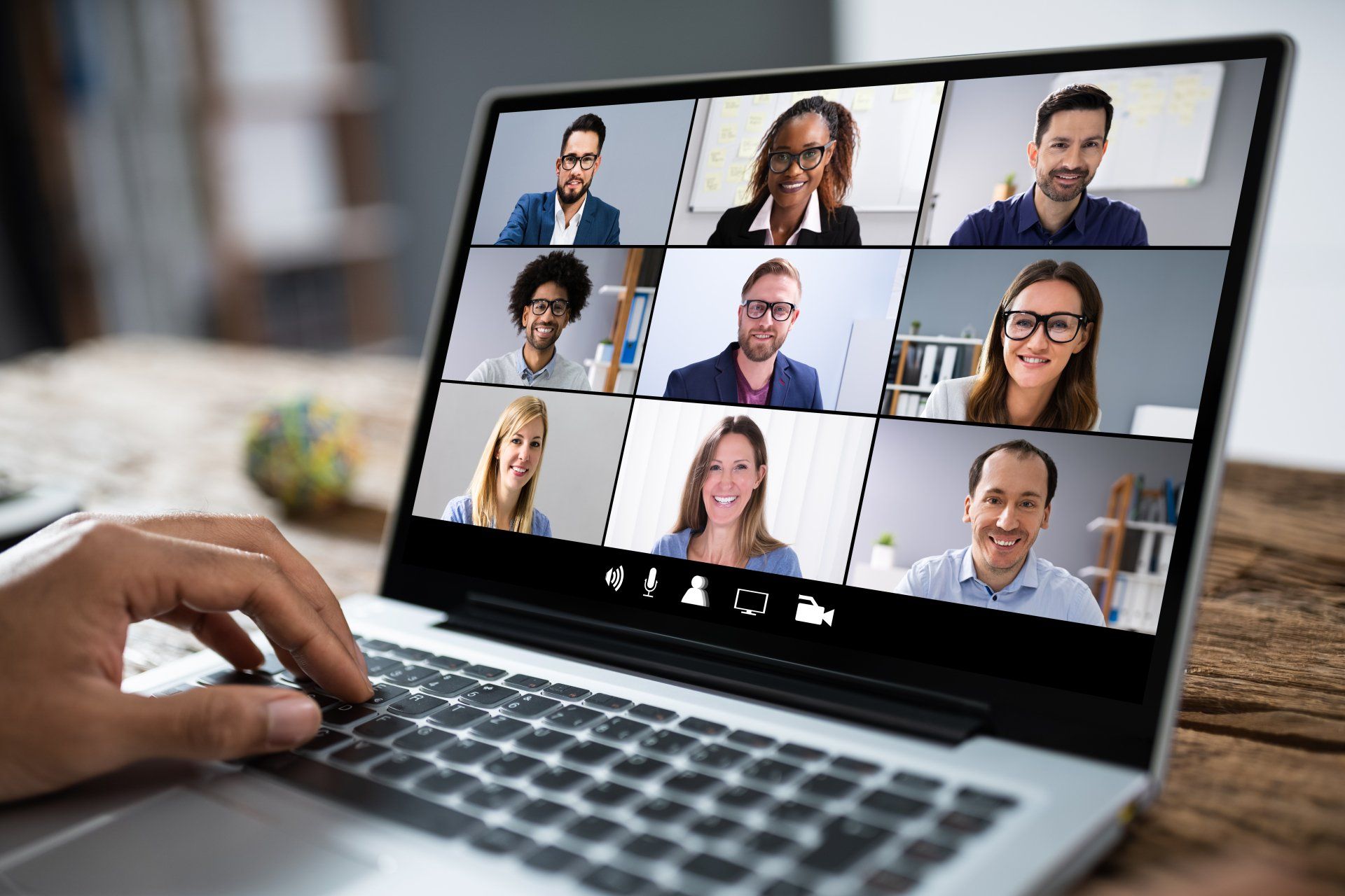 Video conference on a laptop with nine participants in tiled view on a desk