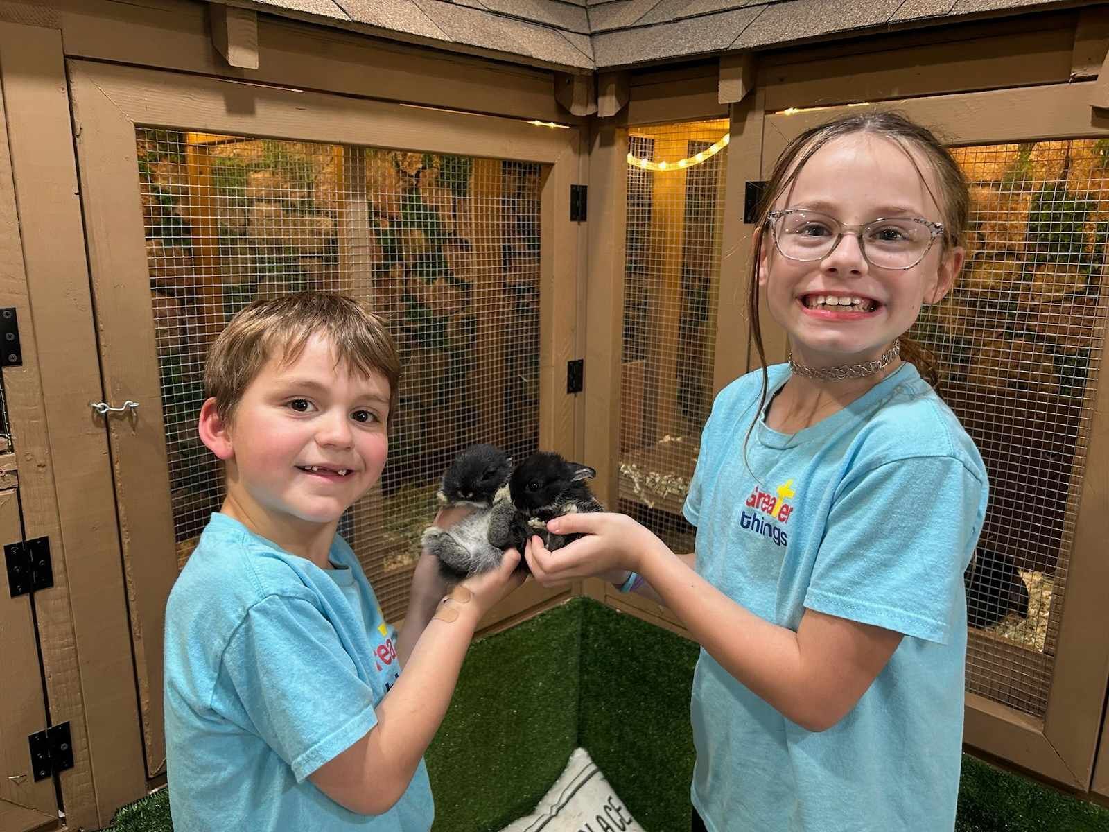 A boy and a girl are holding a kitten in a cage.