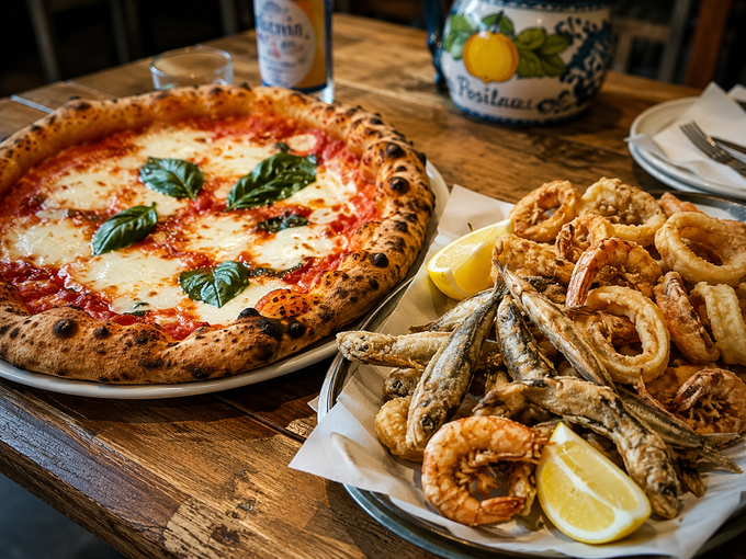 Pizza napoletana e piatto di frutti di mare fritti con spicchi di limone su un tavolo di legno