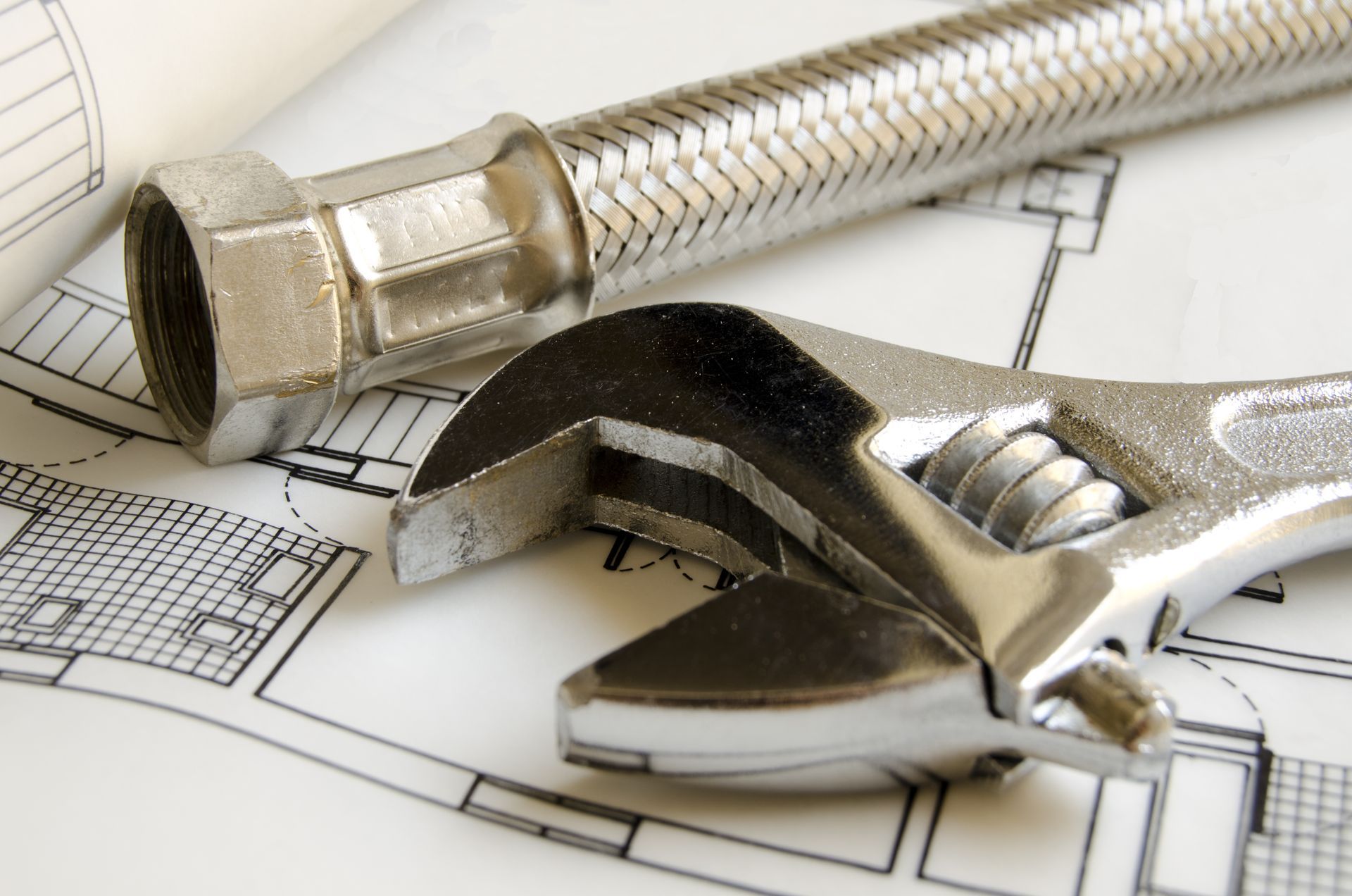 Plumber fixing under-sink pipes while a homeowner watches in a bright white kitchen