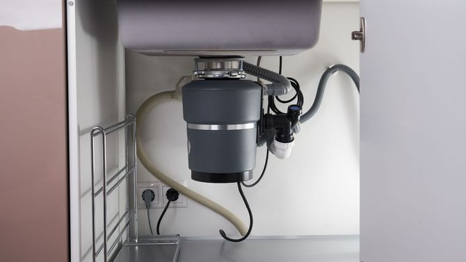 Under-sink garbage disposal with exposed plumbing and power cord in a cabinet