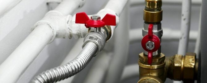 Close-up of red-handled plumbing valves and silver flexible hose on white pipes