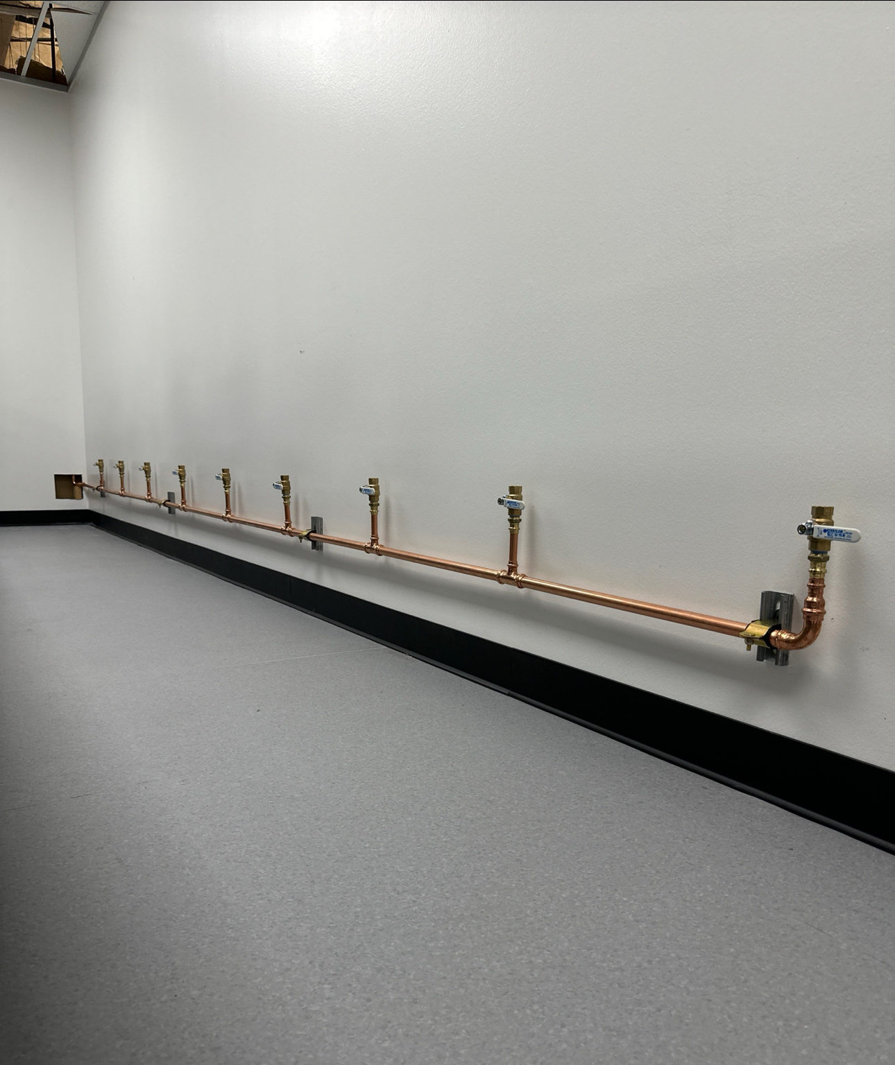 Row of copper pipes and valves along a white wall in a utility room