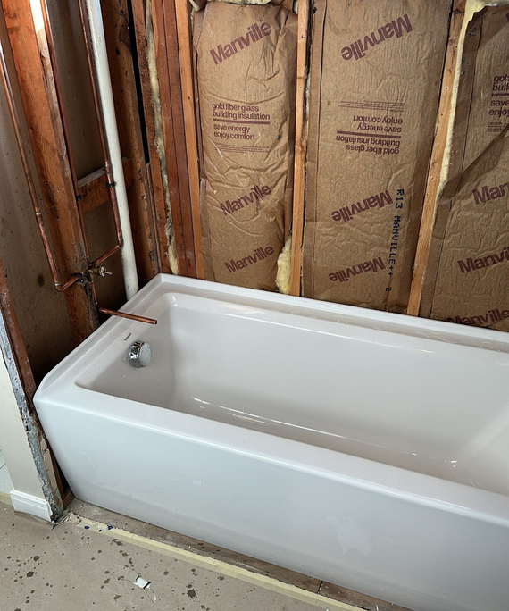 White bathtub in unfinished bathroom with exposed insulation and drywall around it