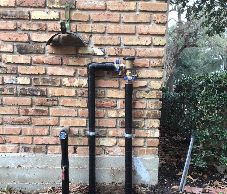 Brick wall with black utility pipes and a small wall-mounted light fixture outdoors.