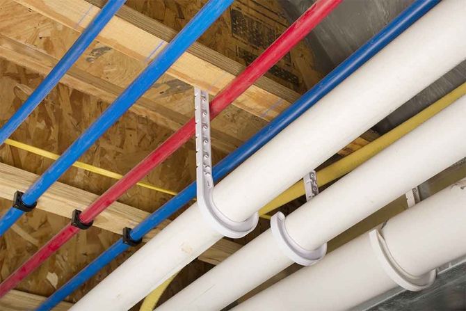 Color-coded ceiling pipes and conduits running across an unfinished construction ceiling
