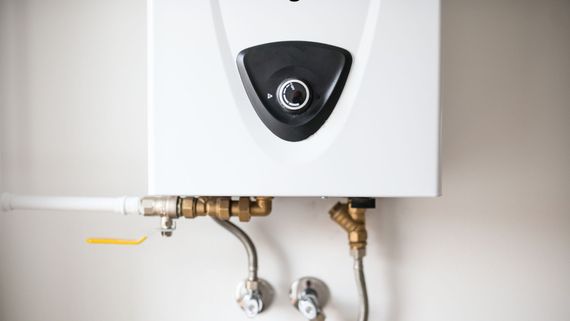 White wall-mounted water heater with exposed pipes and valves underneath