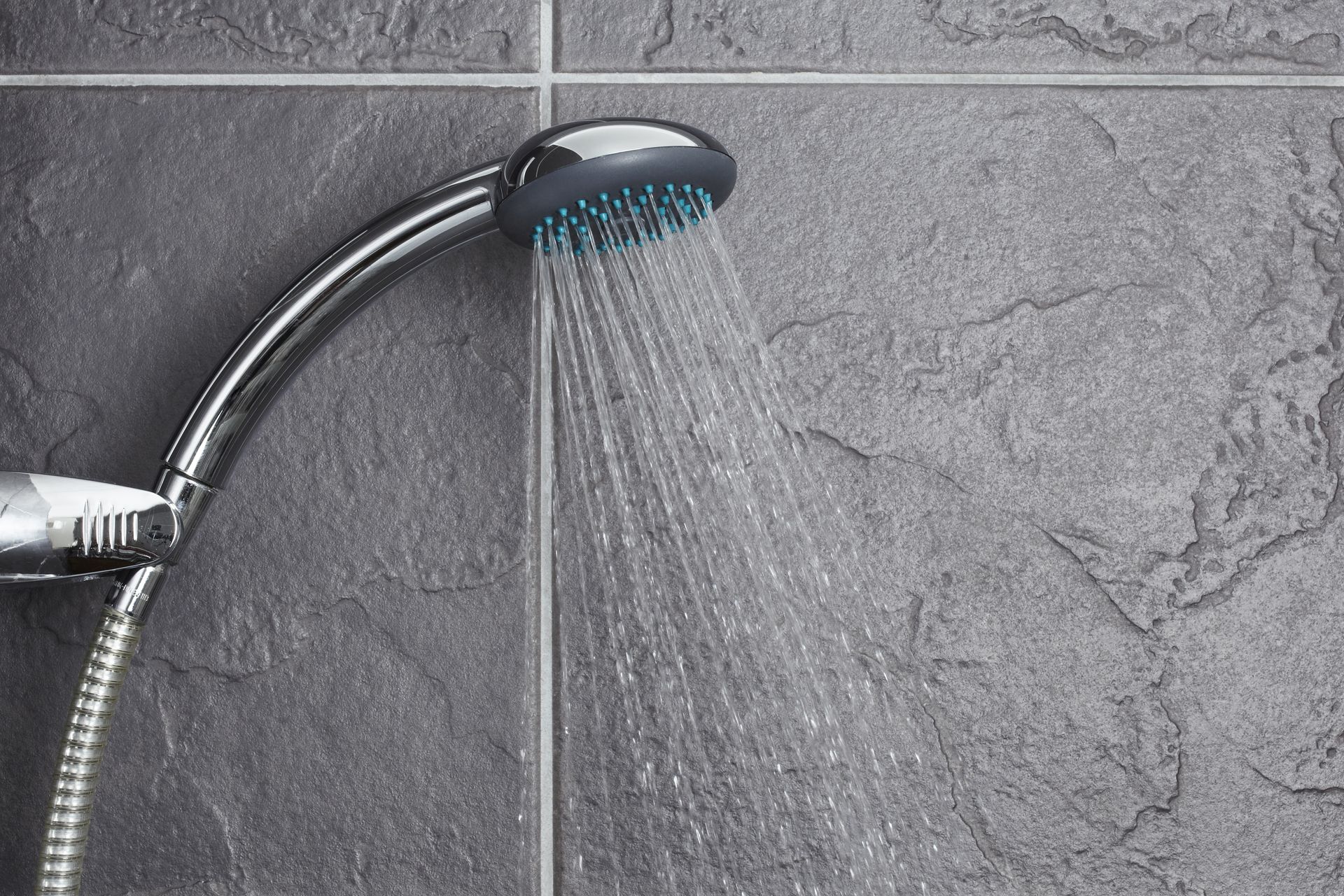 Chrome showerhead spraying water on gray tiled bathroom wall