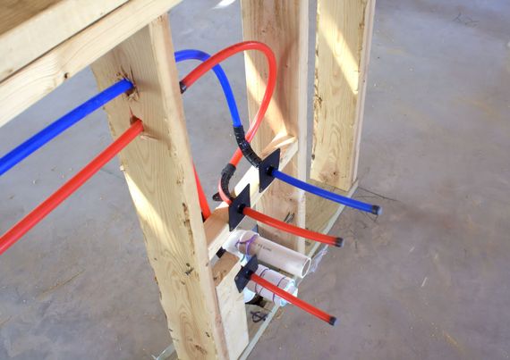Plumbing pipes and fittings installed between wooden wall studs on a concrete floor.