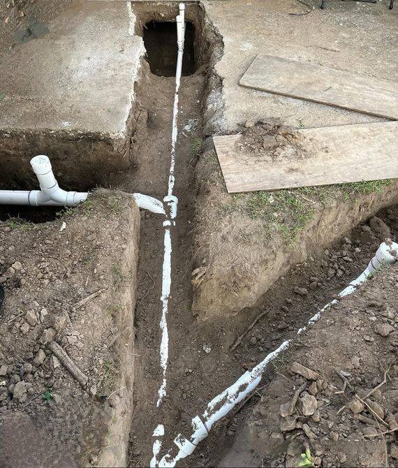 Open trench with white PVC pipes and fittings beside concrete slabs during utility work