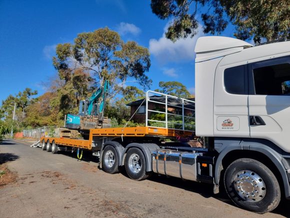 excavator machines being transported on a flatbed truck