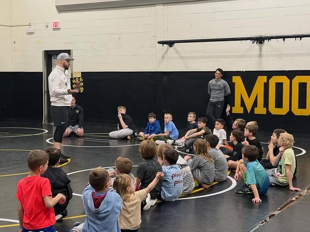Coach speaking to seated children in a gymnasium during a sports lesson