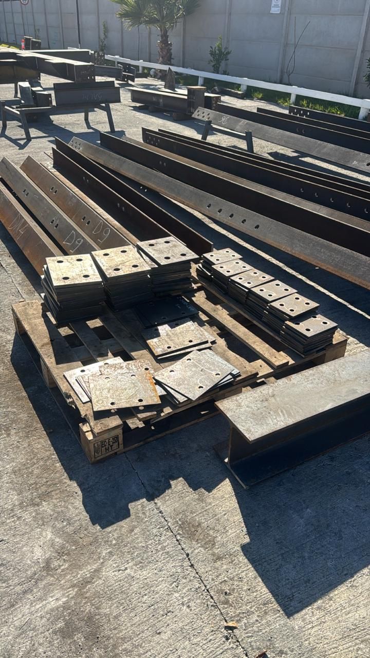 Vigas metálicas, placas y otros materiales de construcción apilados en palets al aire libre.