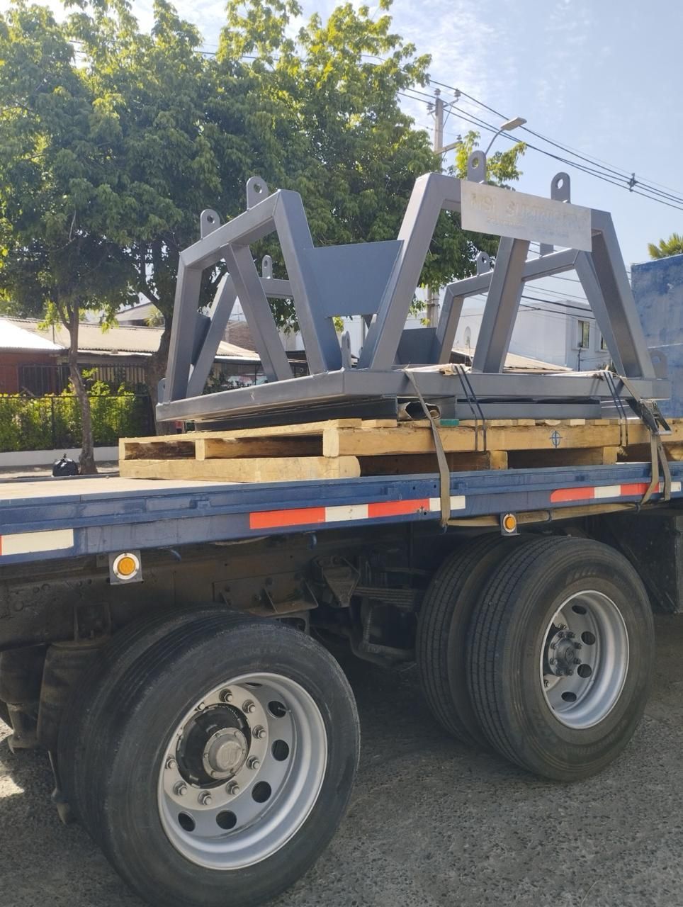 Marco de metal gris sobre paletas de madera fijado a una plataforma de camión.