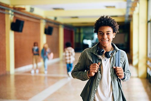 Smiling student with backpack in a school hallway, walking toward the camera