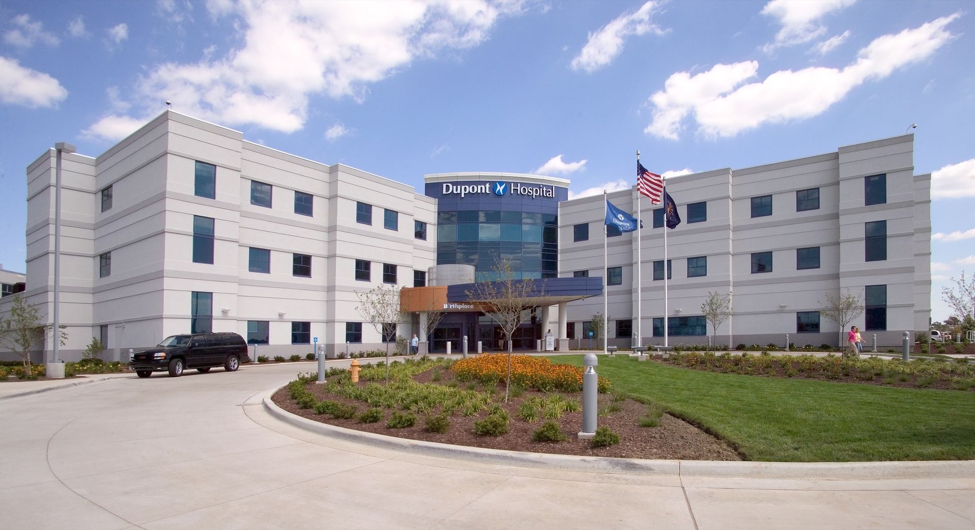 Modern hospital exterior with curved driveway, glass entrance, and flags in front