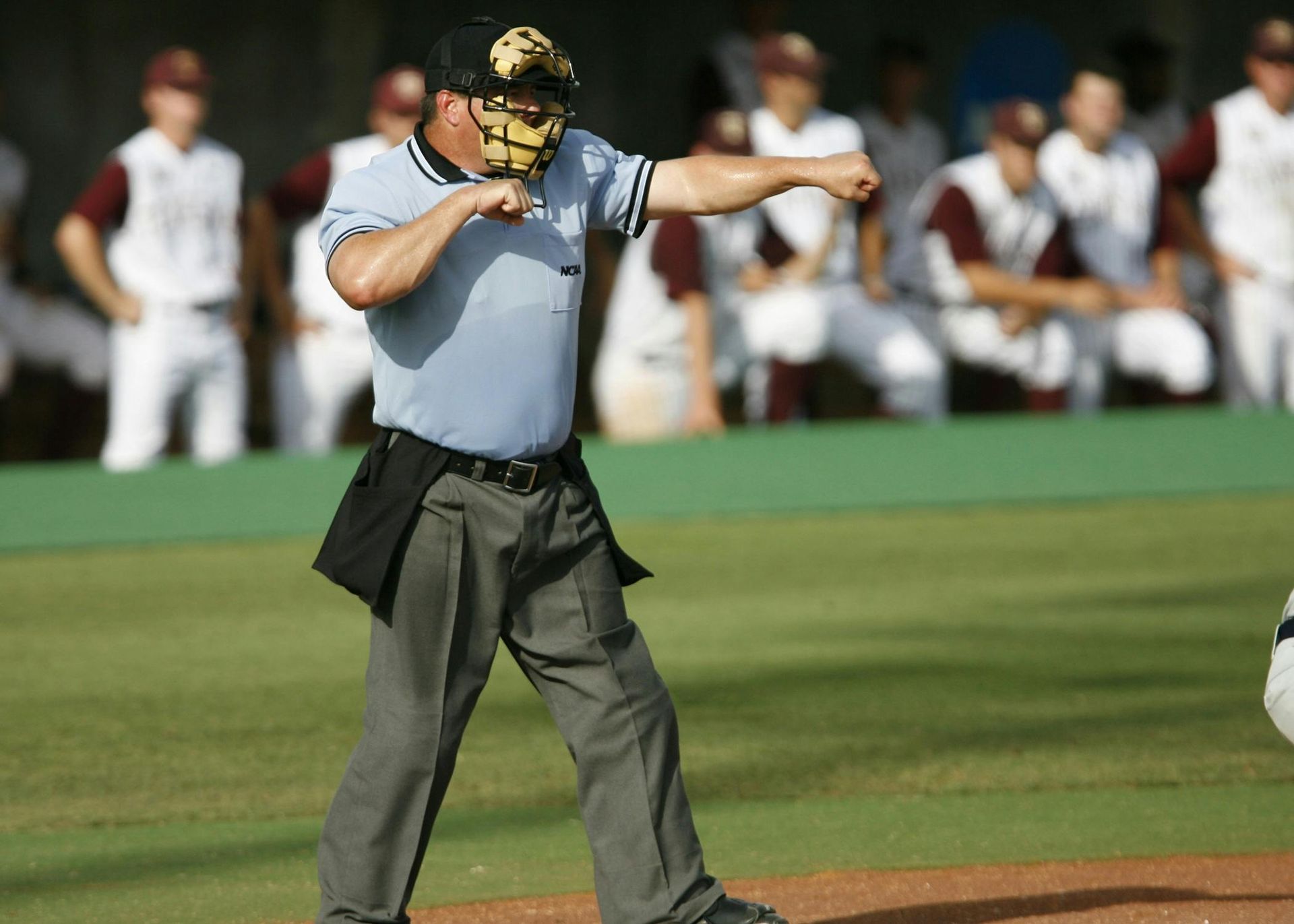 Umpire in gray shirt signals on a baseball field with players blurred in the background